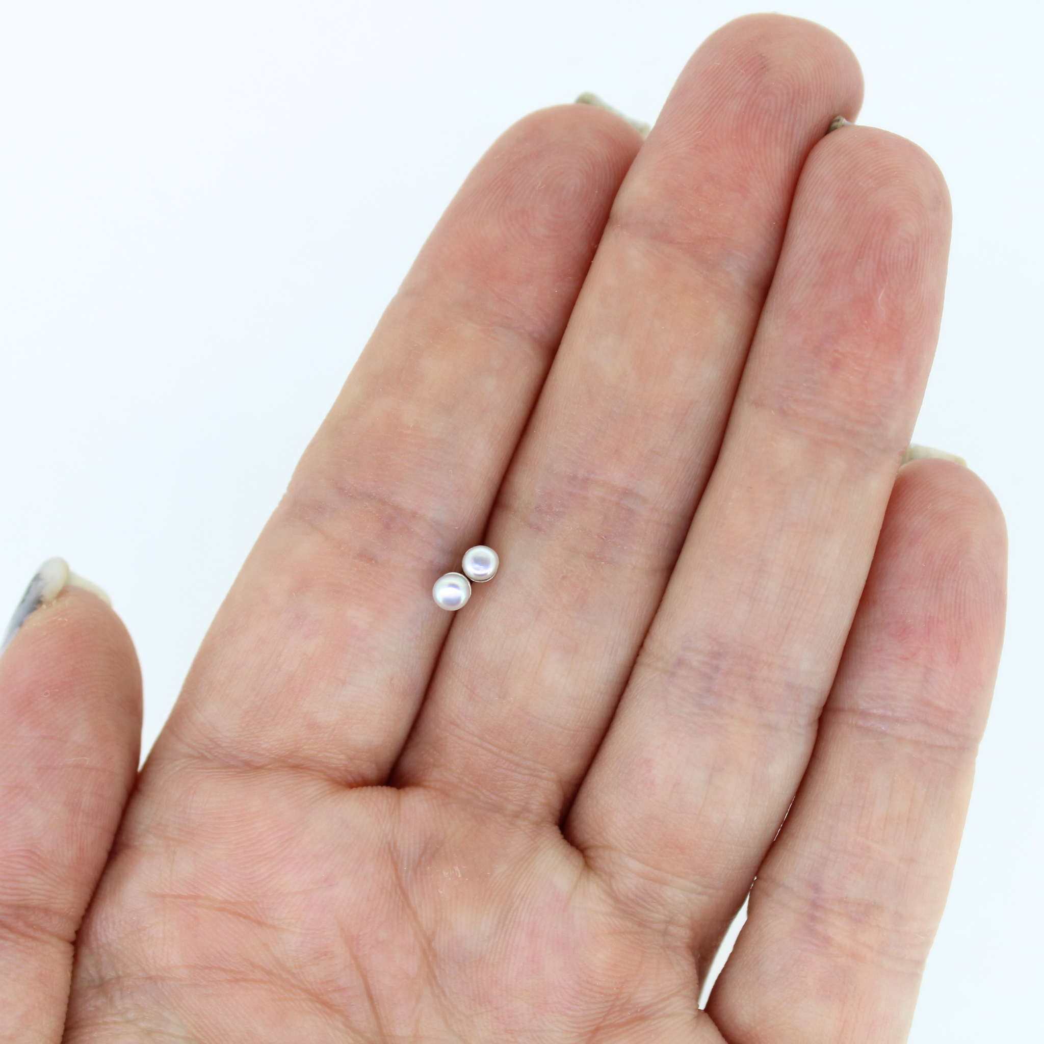 Tiny freshwater pearl stud earrings in sterling silver, pearls shown on hand