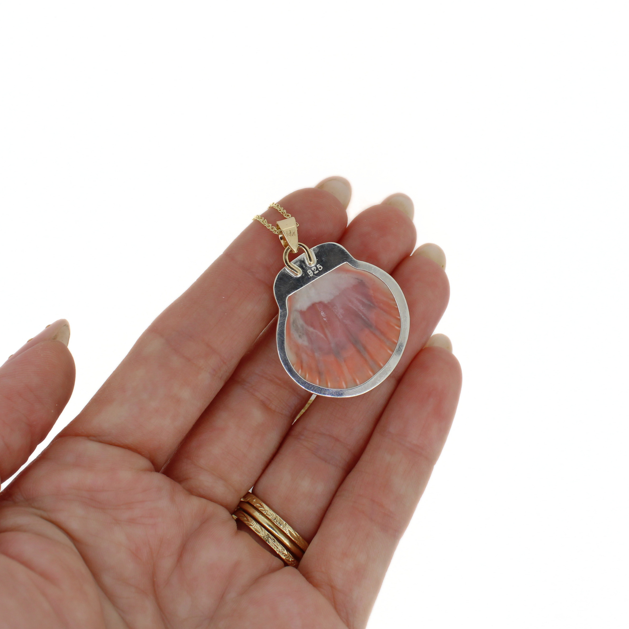 Shell pendant necklace with silver-toned frame and pink swirls, held in hand