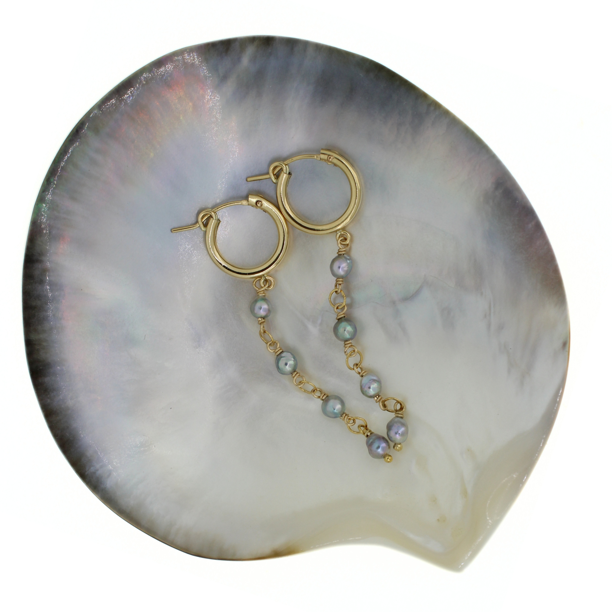 Gold hoop earrings with dangling chains of small iridescent akoya pearls, displayed on a large iridescent shell against a white background. Handmade by Brianne & Co. in Kauai, Hawaii