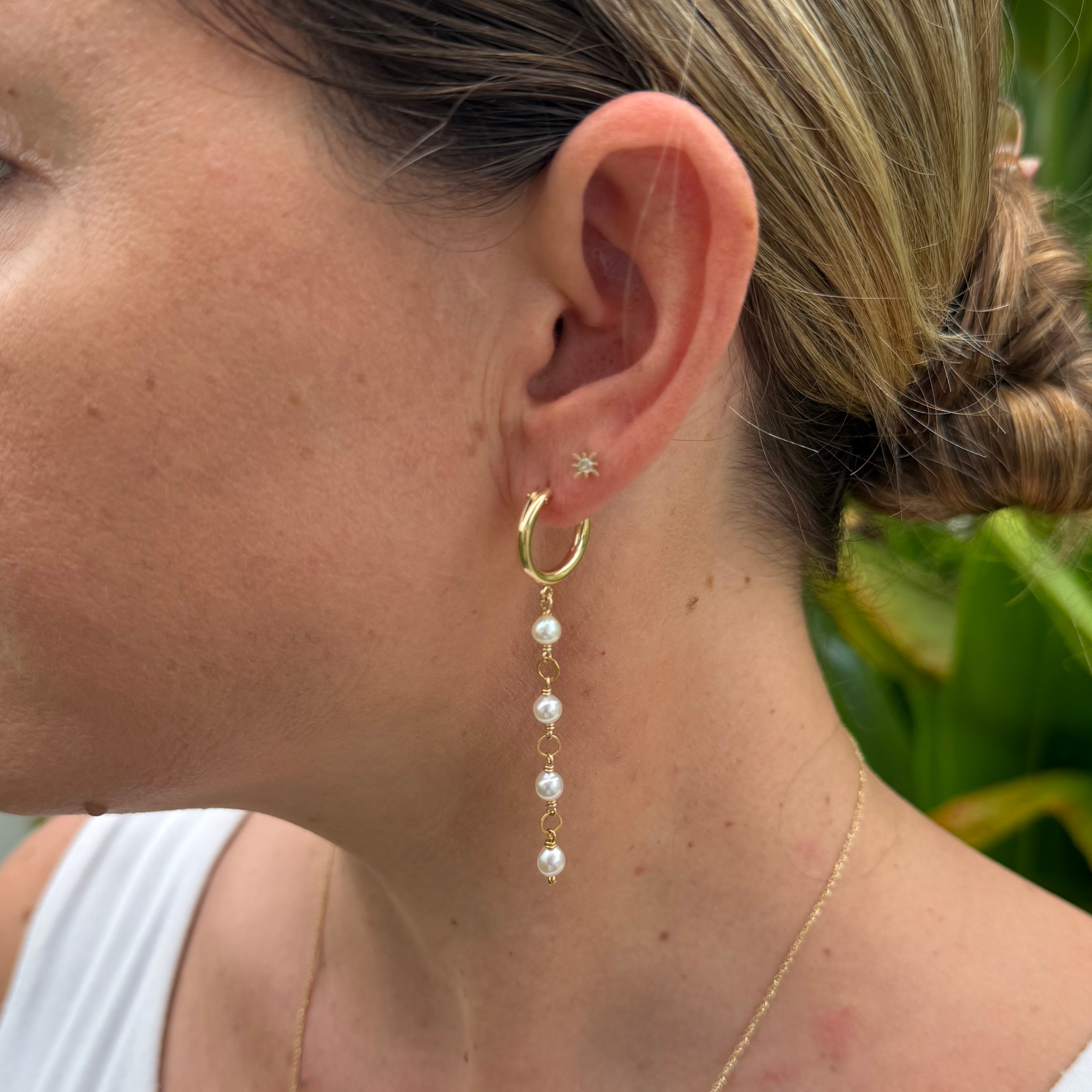 A close-up of a woman's ear wearing a small gold hoop earring with four small white pearls.