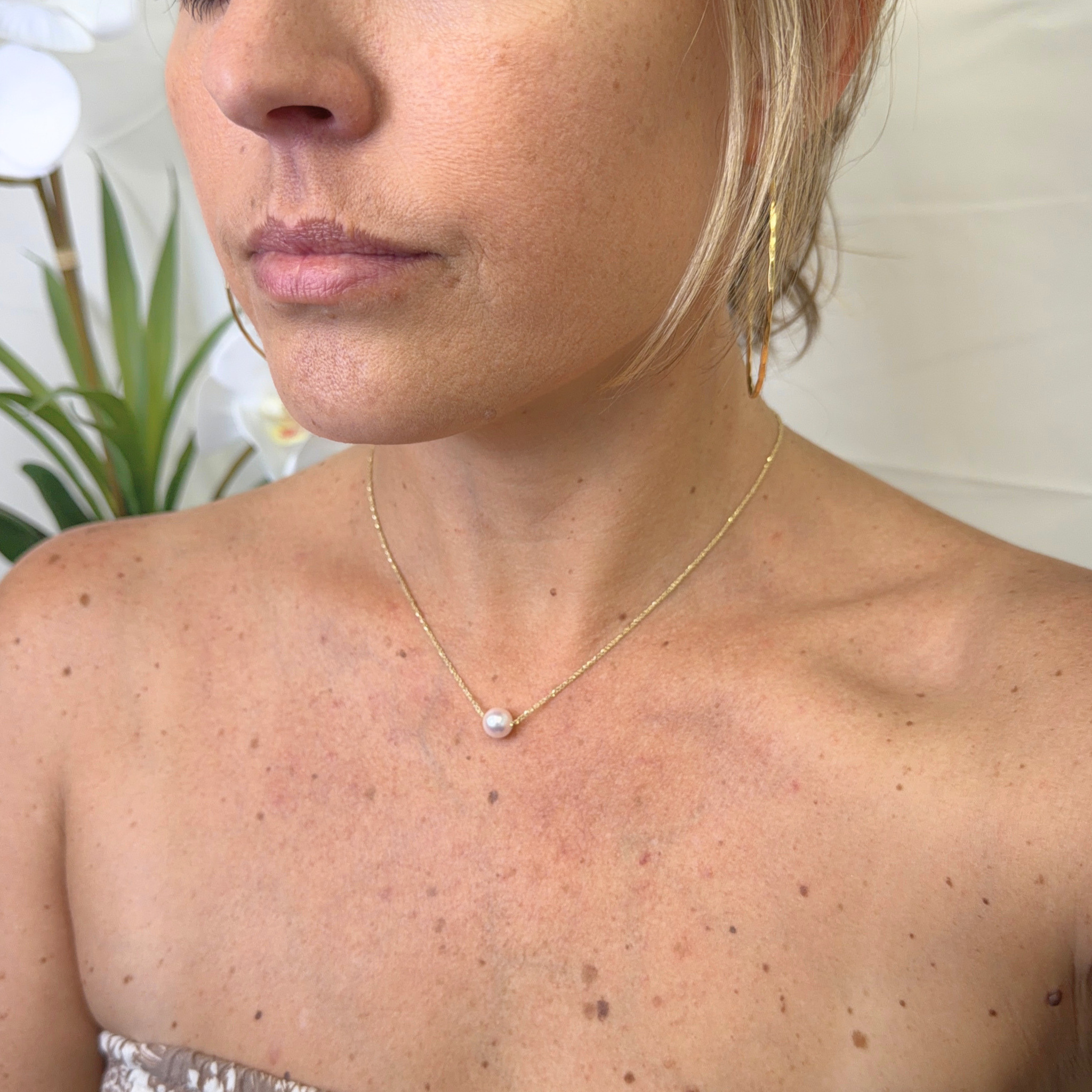 A close-up lifestyle shot of a woman wearing a delicate gold chain necklace with a single white pearl pendant, shown against her neck and upper chest.