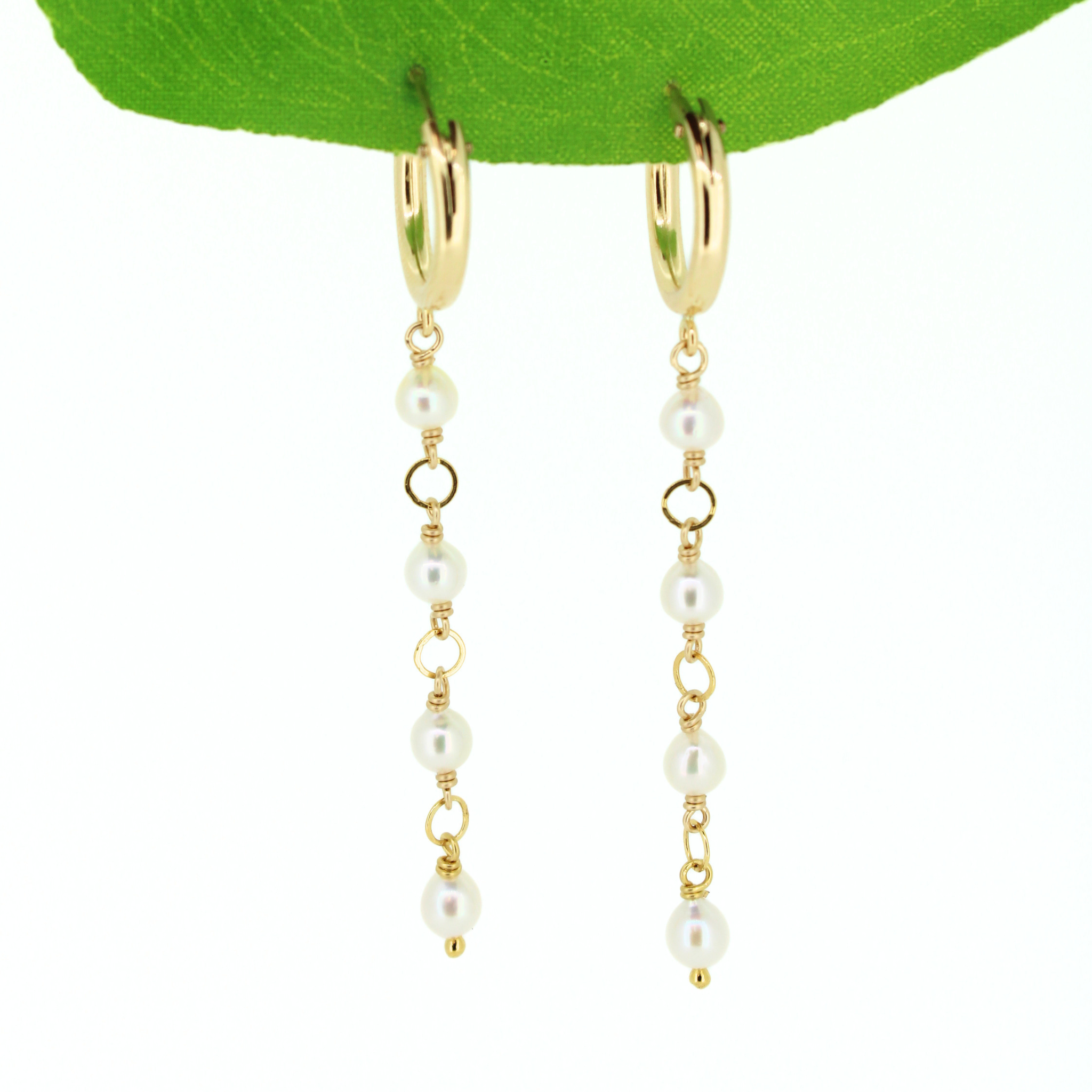 A pair of gold hoop dangle earrings with tiny white akoya pearls and small gold spacer rings, hanging from a green leaf against a white background. Handmade in Kauai, Hawaii by Brianne & Co.