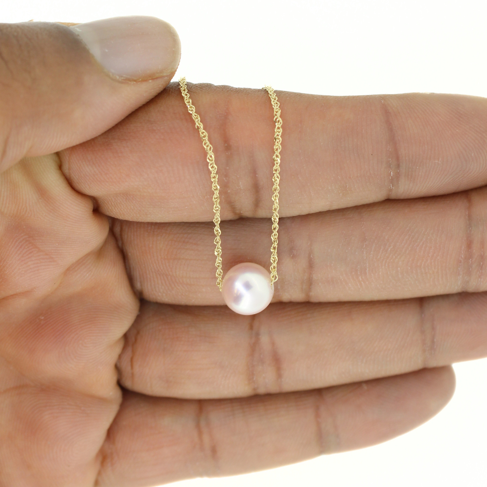 A delicate gold chain necklace with a single round white pearl pendant, held in the palm of a hand against a white background.