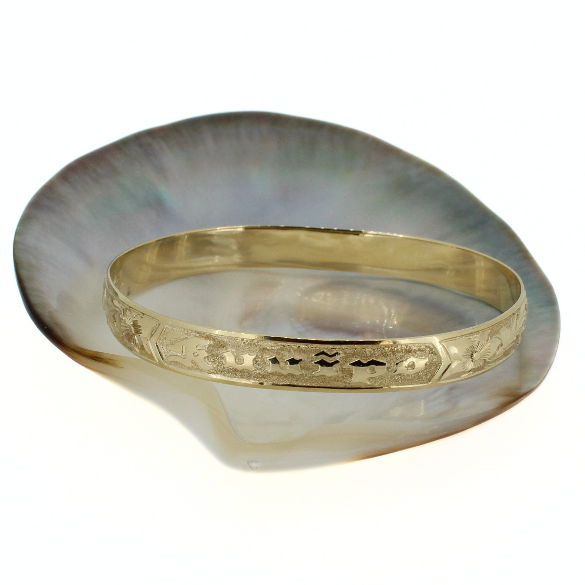 Gold bangle shown on a tray, engraved ocean-inspired and floral details on band