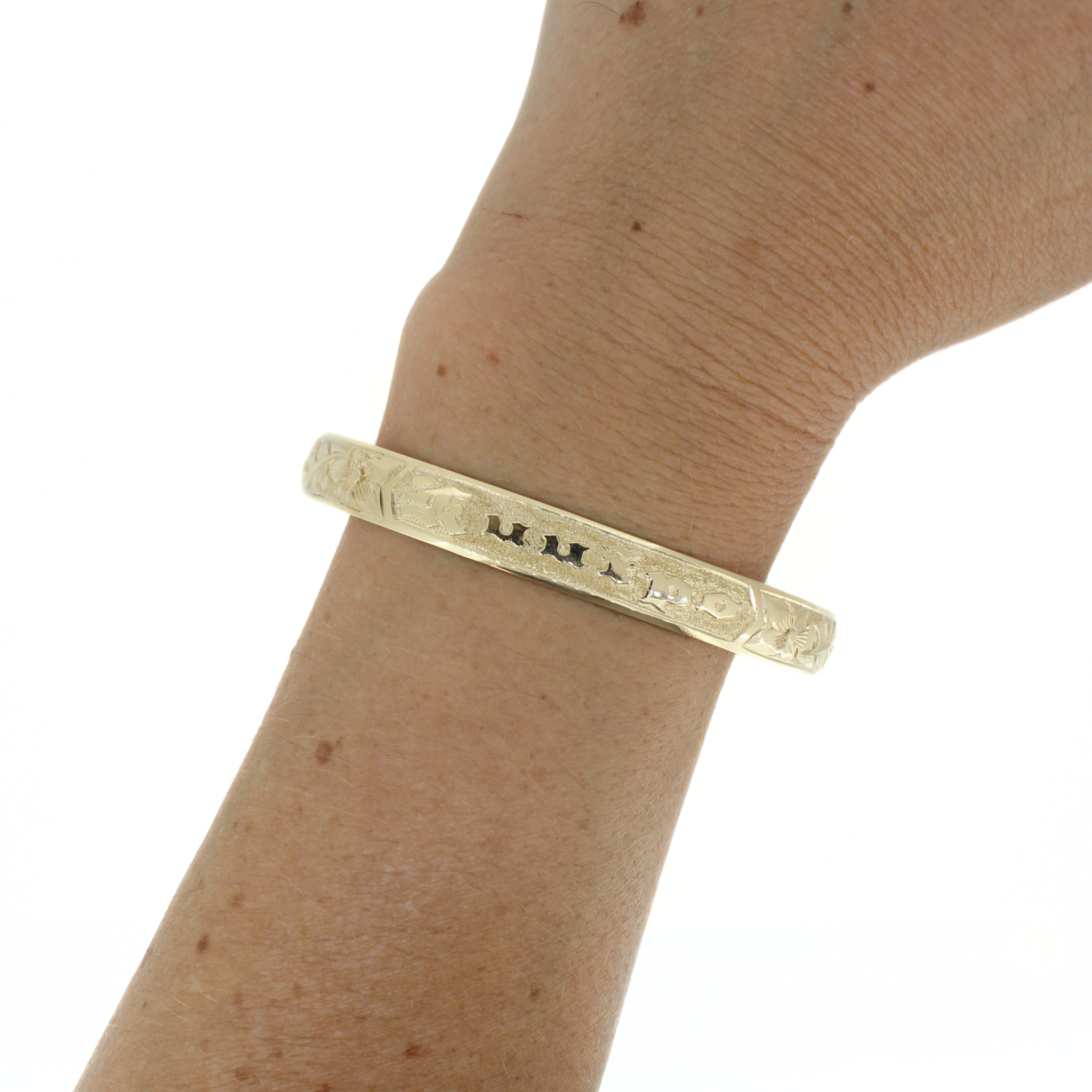 Gold bangle on wrist, engraved tropical motifs across the front band