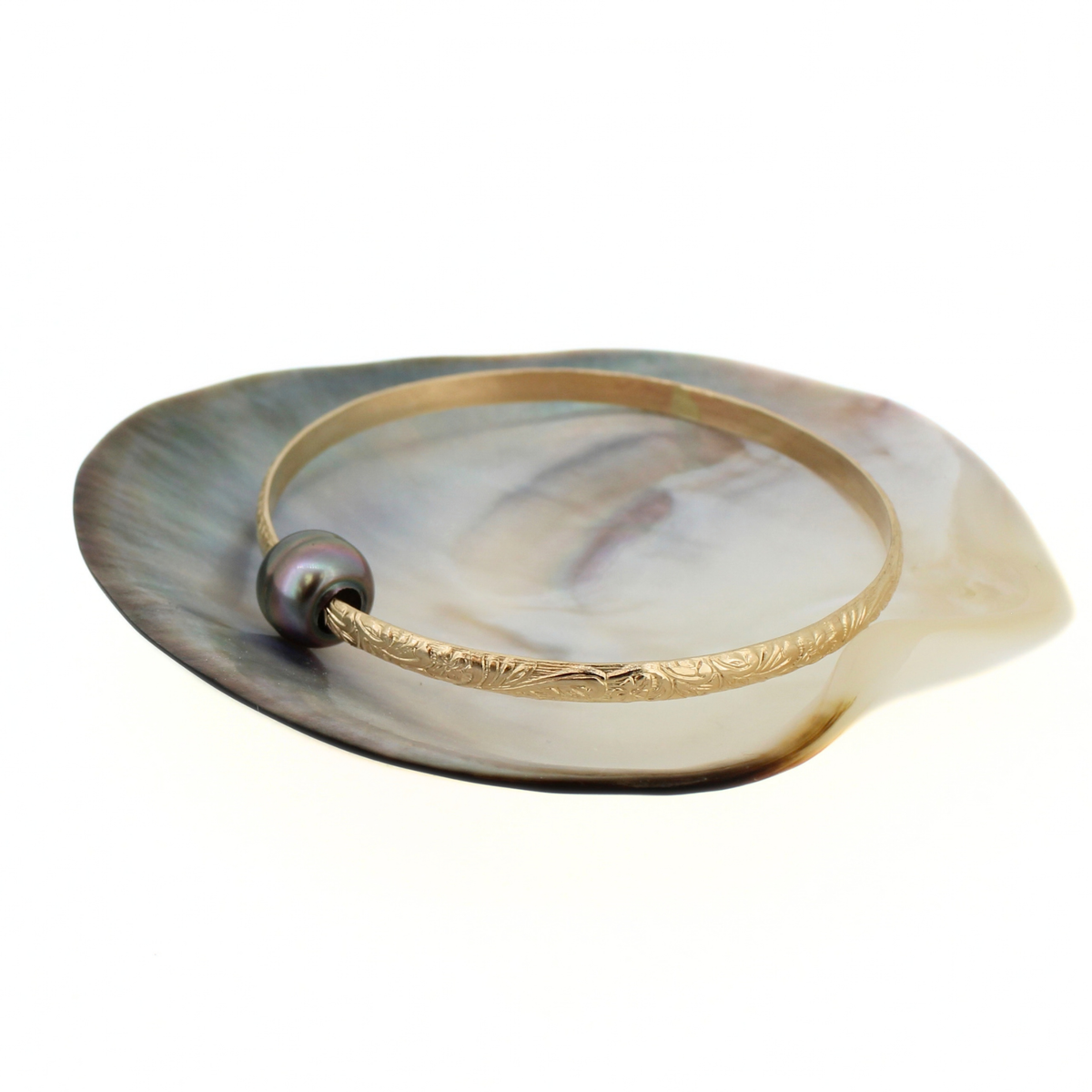Gold Tahitian pearl bangle bracelet displayed on a mother of pearl shell