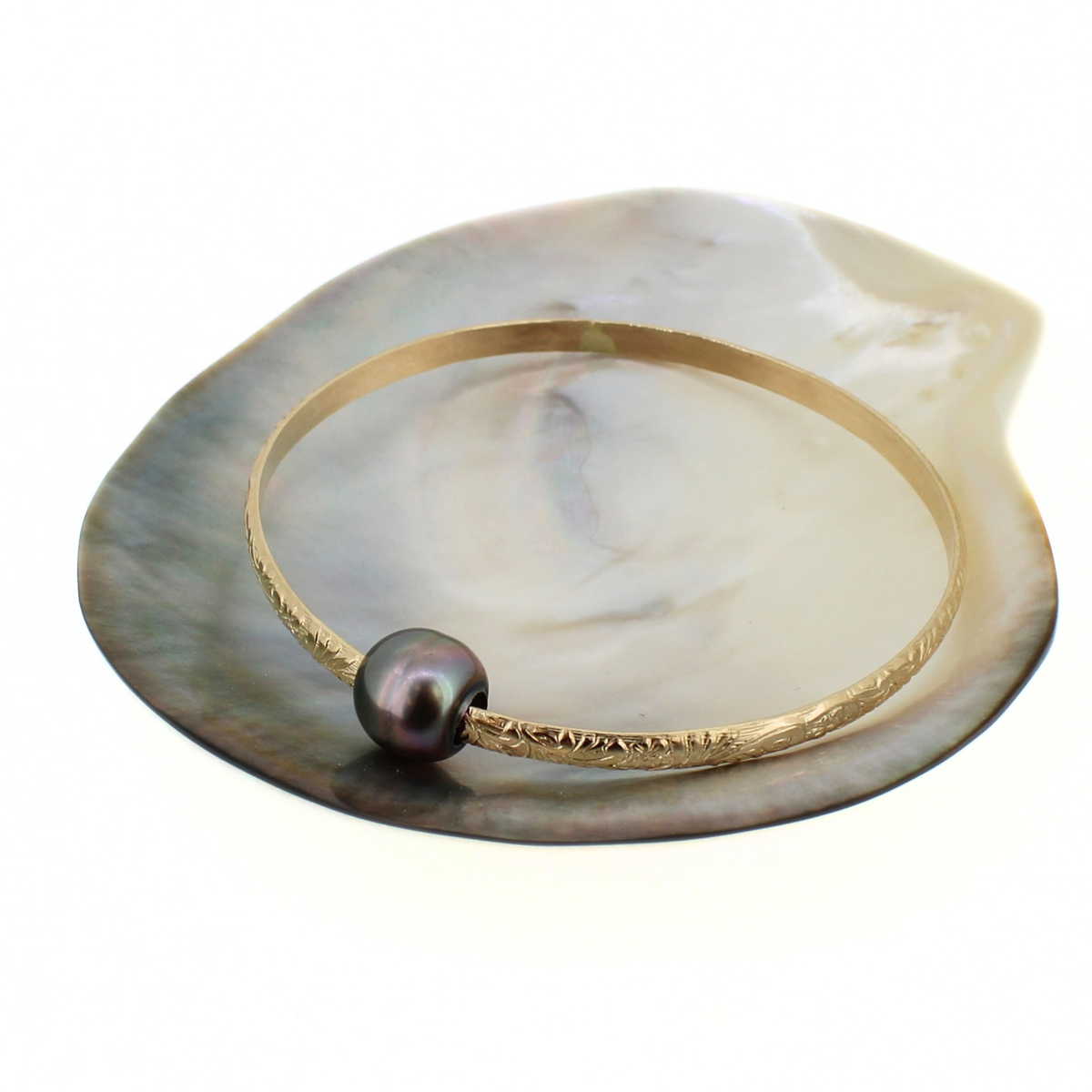 Gold bangle bracelet with a dark Tahitian pearl displayed against a mother of pearl shell