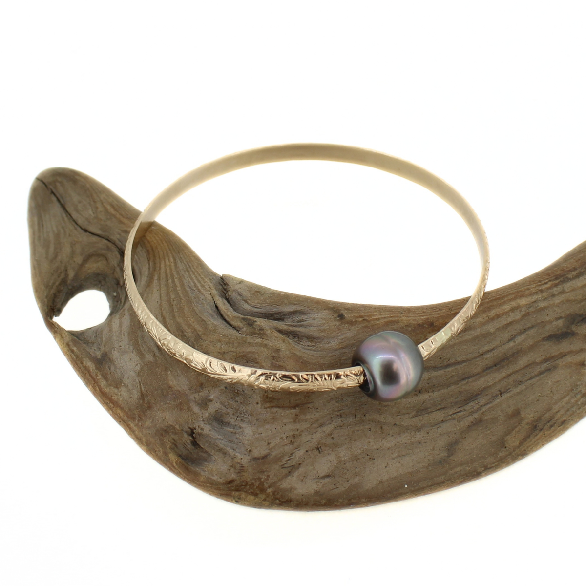 Gold Tahitian pearl heirloom style bangle bracelet shown on a piece of driftwood