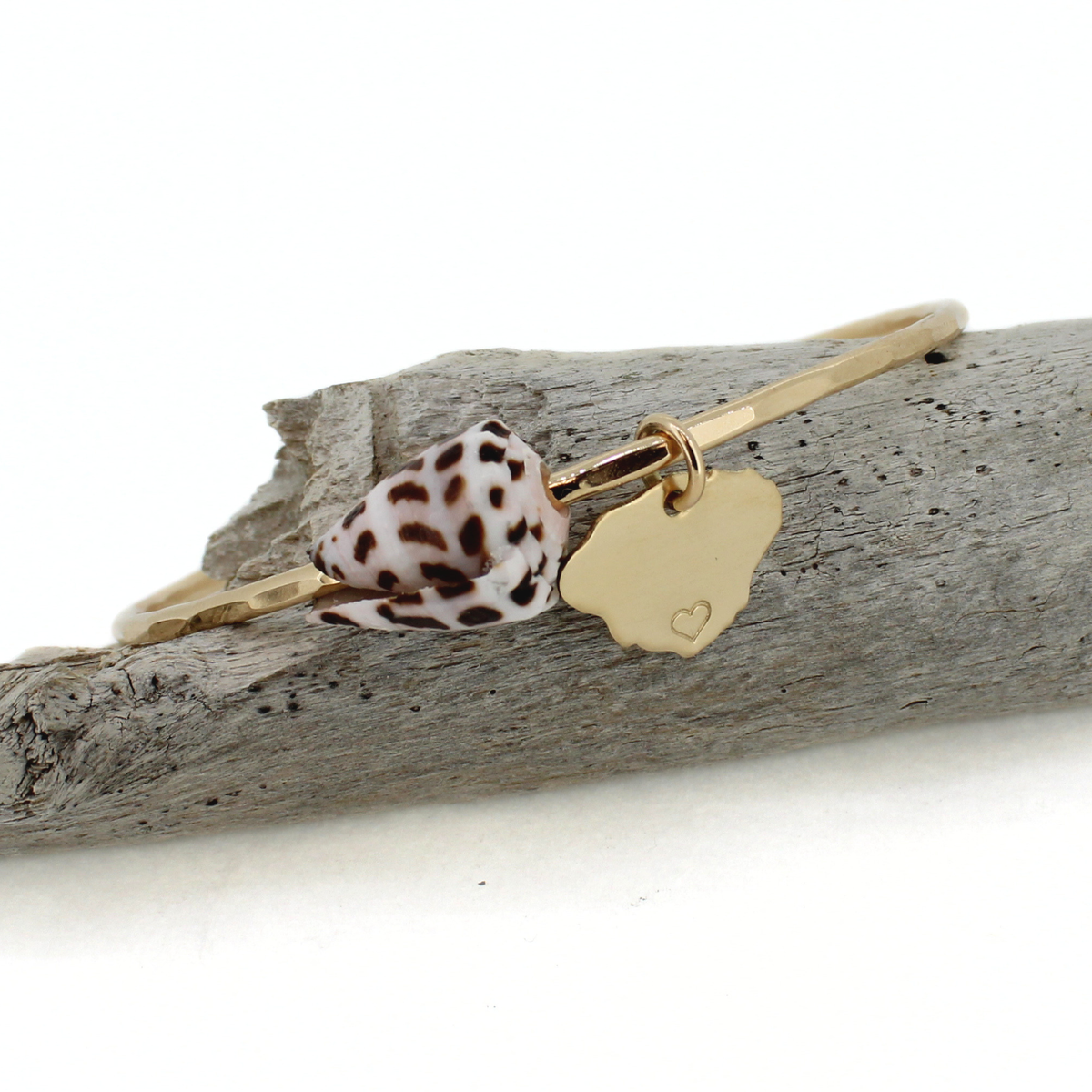 Gold bangle bracelet with a hammered texture featuring a cone shell and kauai island charm