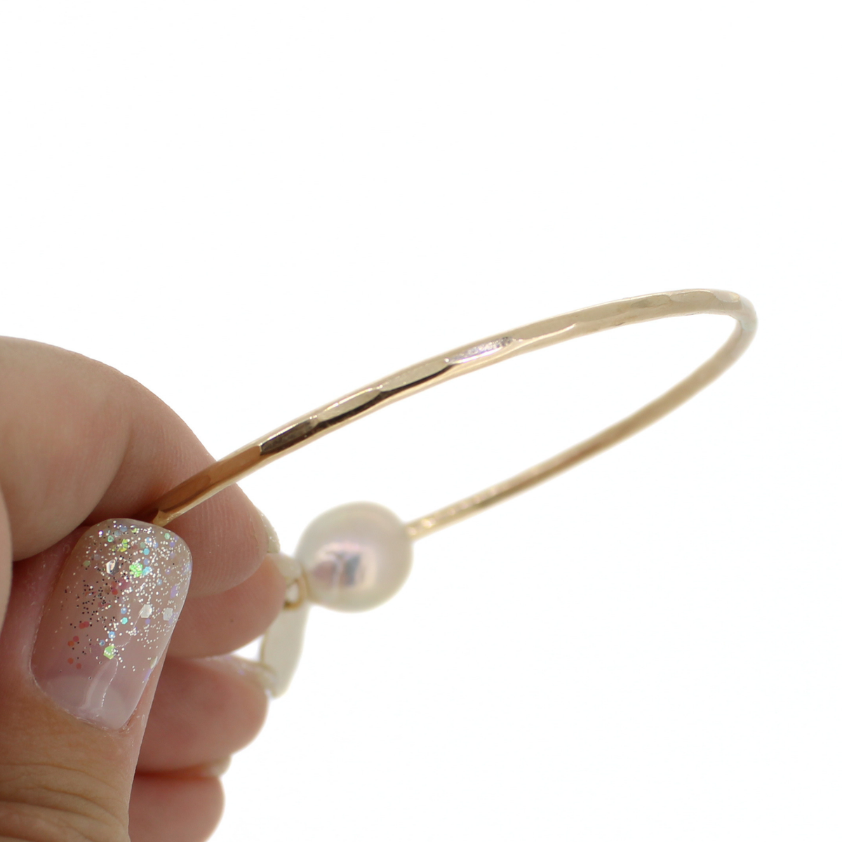A close-up of a hand holding a slim gold bangle bracelet with a hammered texture, against a plain white background.