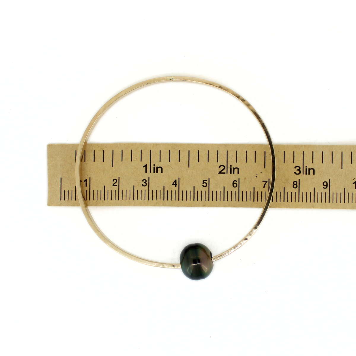 Gold Tahitian pearl bangle bracelet shown over a paper ruler for size reference