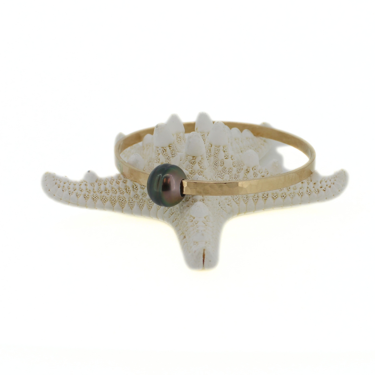 Gold Tahitian pearl bangle bracelet displayed on a starfish against a white background