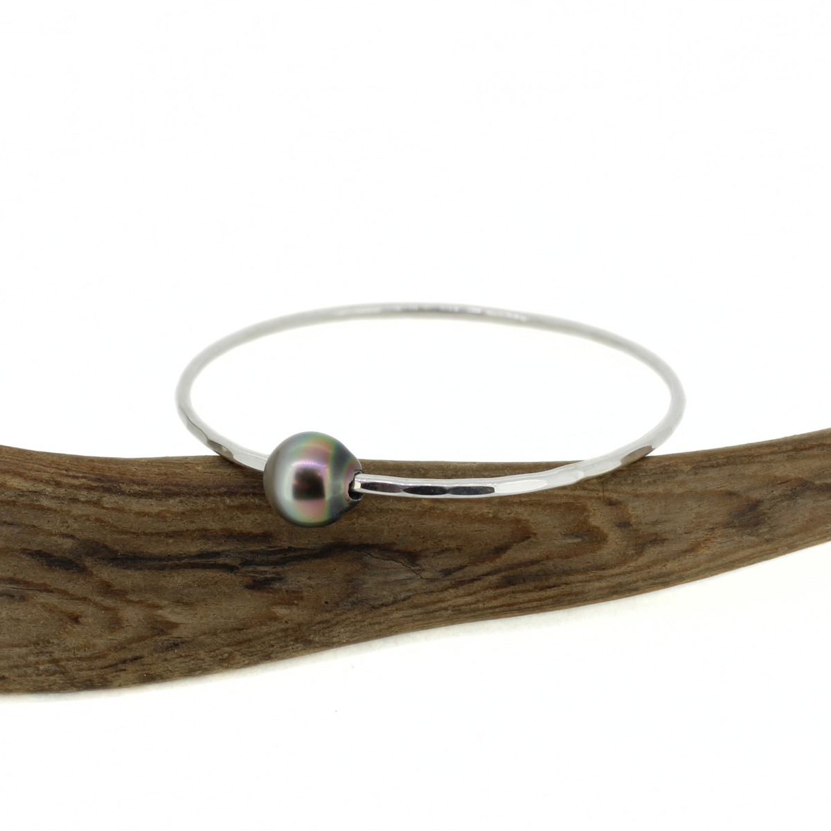 Sterling silver hammered bangle bracelet with a genuine Tahitian pearl displayed on a piece of driftwood