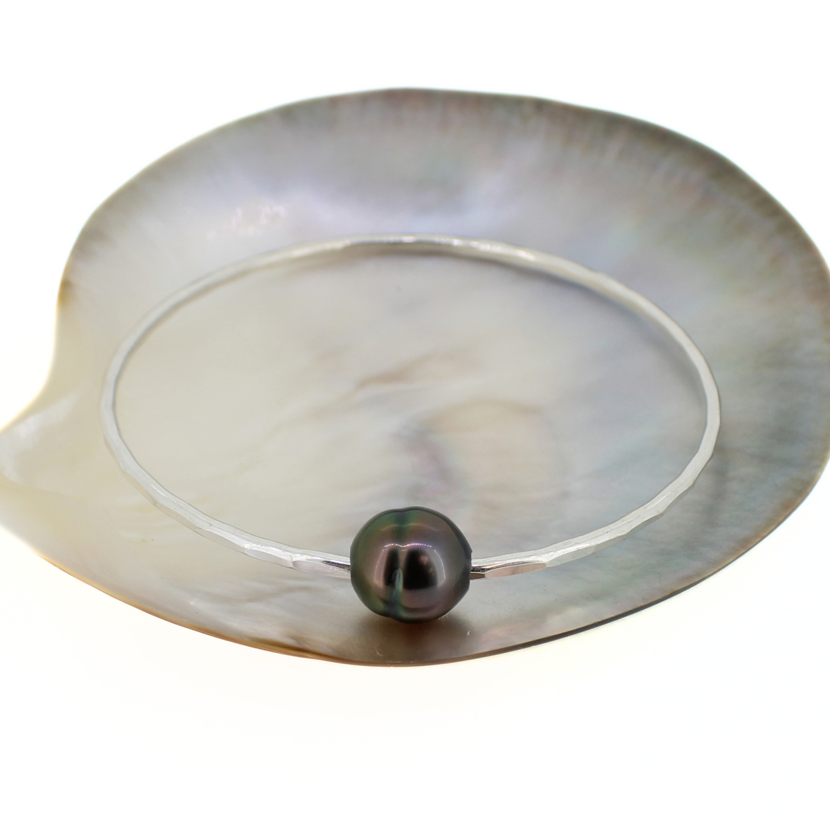 Silver round bangle bracelet with a Tahitian pearl displayed on a mother of pearl shell