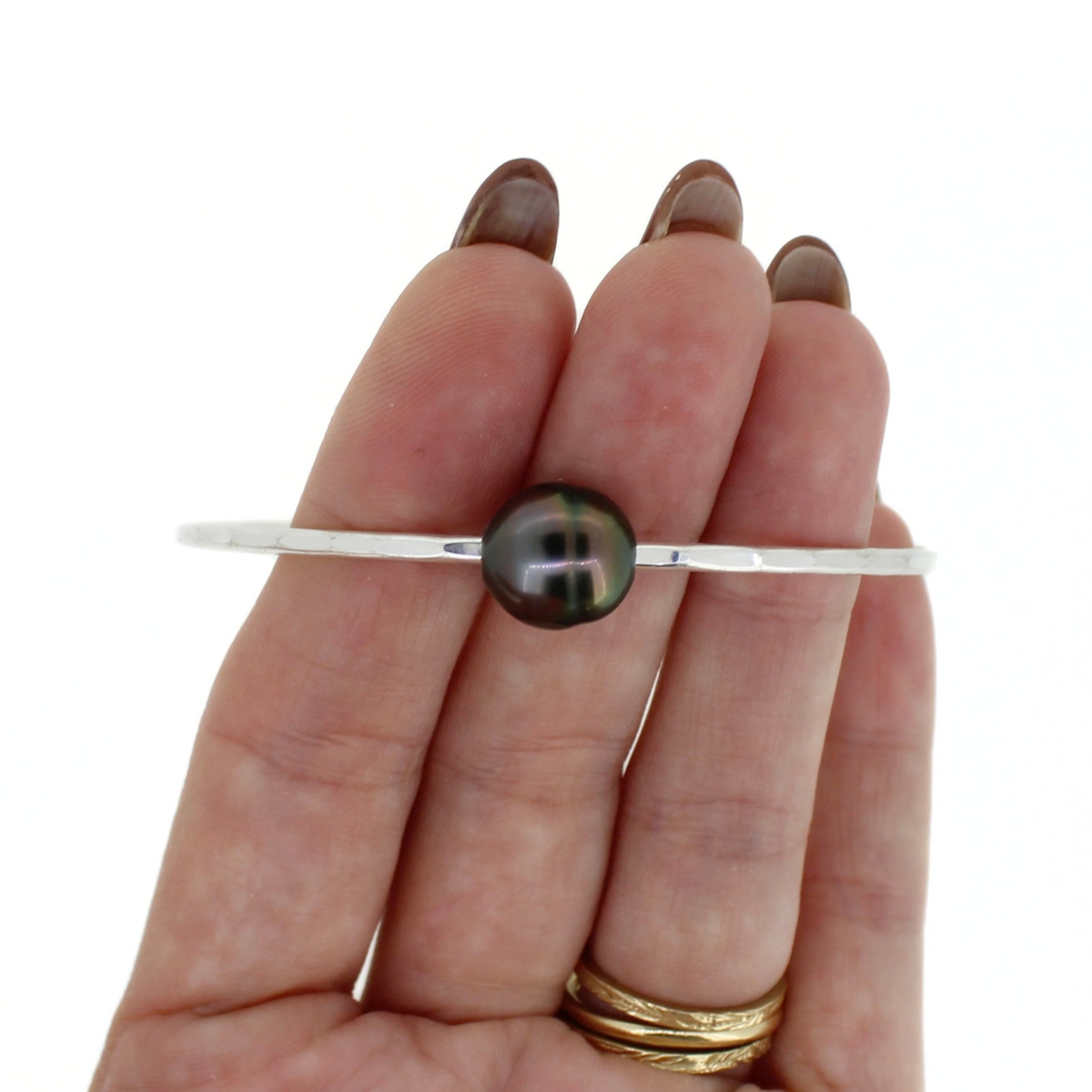 Silver hammered bangle bracelet with a dark gray Tahitian pearl shown on a persons fingers against a white background