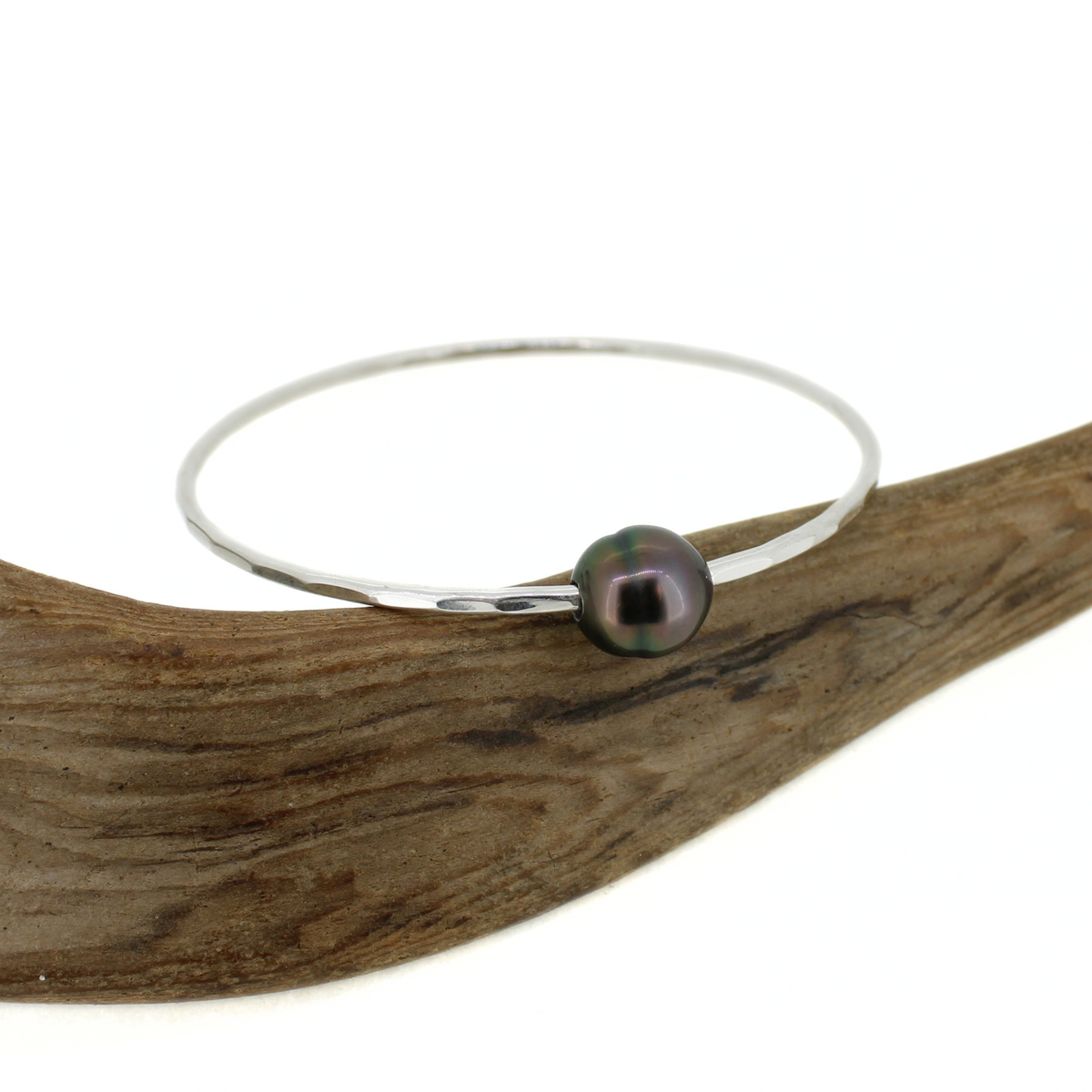 Sterling silver bangle bracelet with a dark gray Tahitian pearl displayed on a piece of driftwood