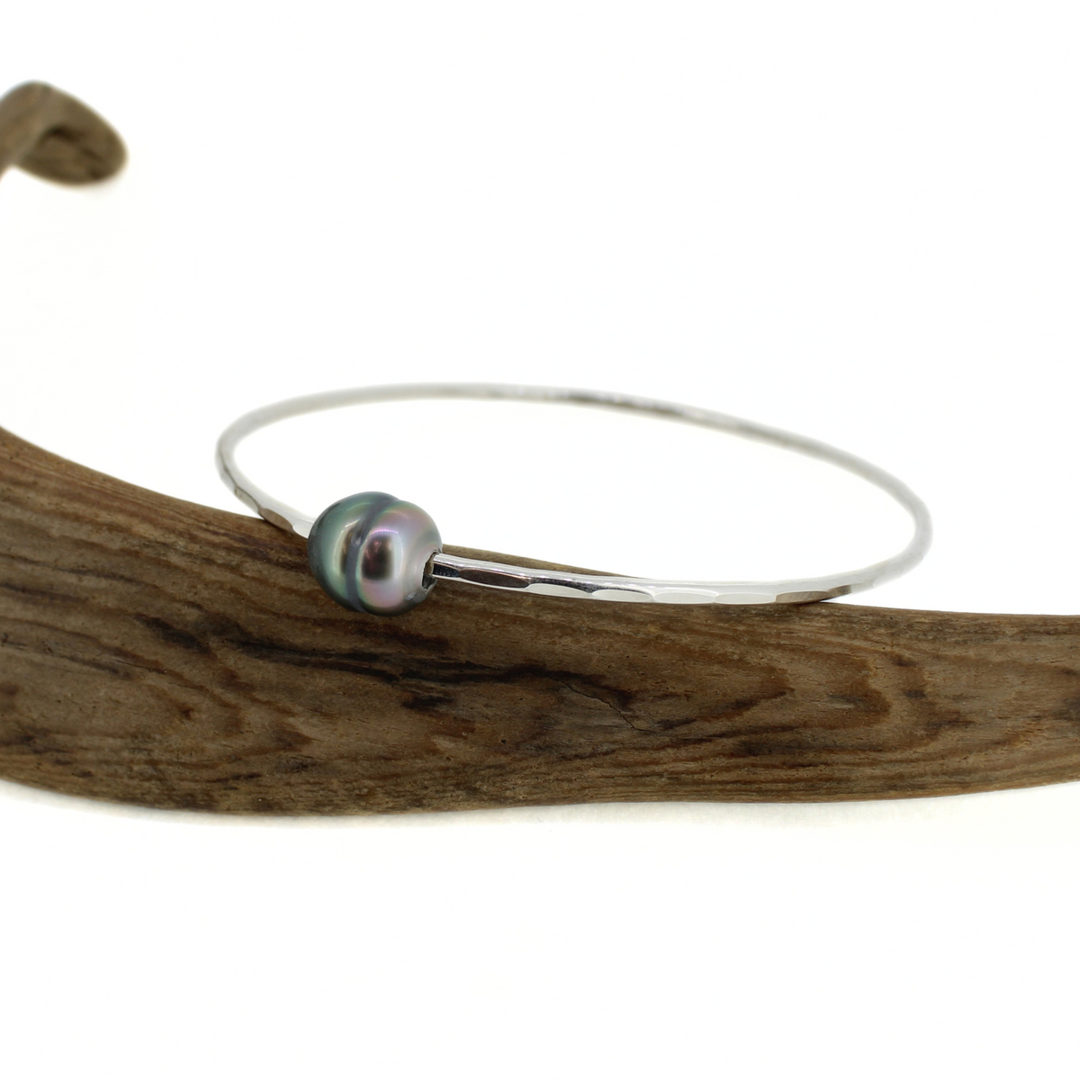 Silver hammered bangle bracelet with a genuine Tahitian pearl displayed on a piece of driftwood