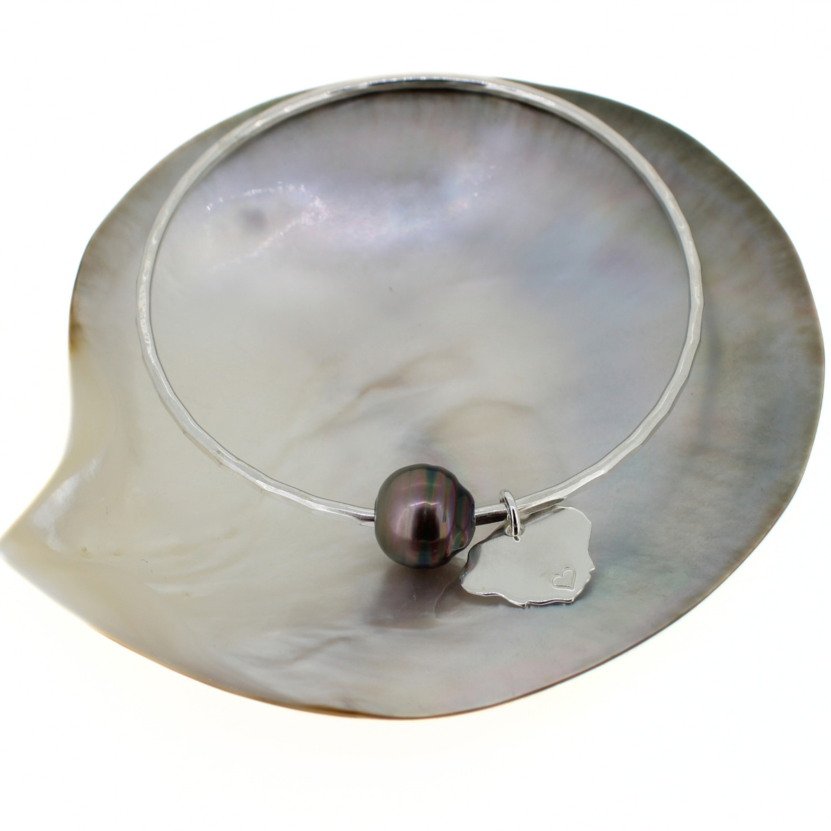 Sterling silver bangle bracelet with a dark Tahitian pearl and a Kauai island charm, displayed on a mother of pearl shell
