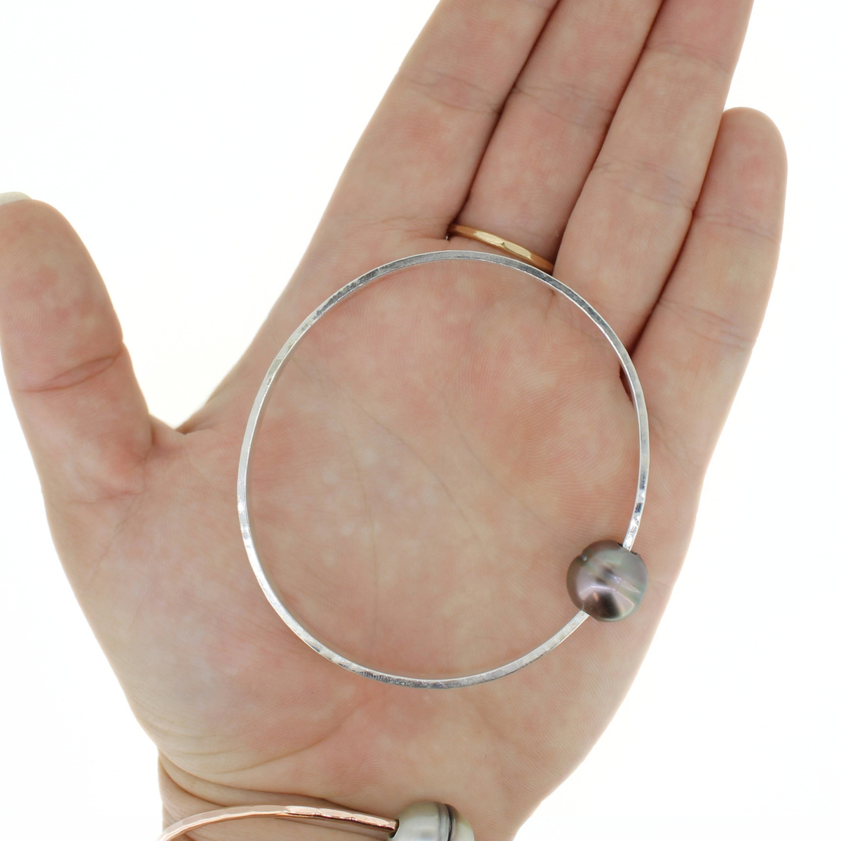 A silver bangle bracelet with a single dark gray pearl, held in a person's hand against a white background.