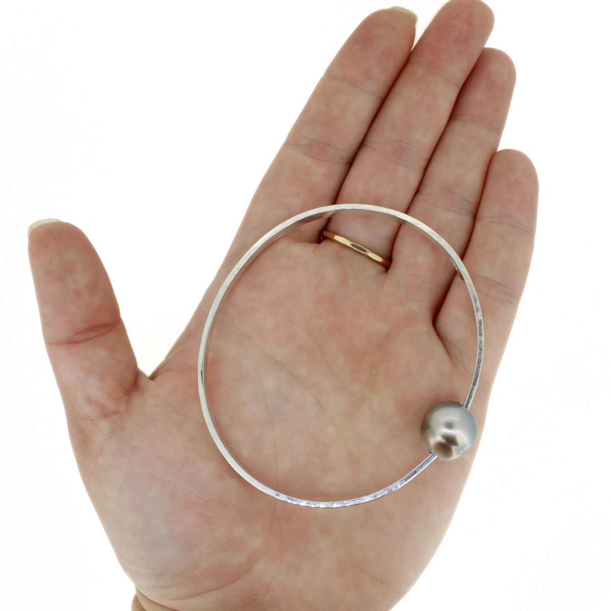 A silver oval bangle bracelet with a single round pearl, shown resting on an open hand for scale.