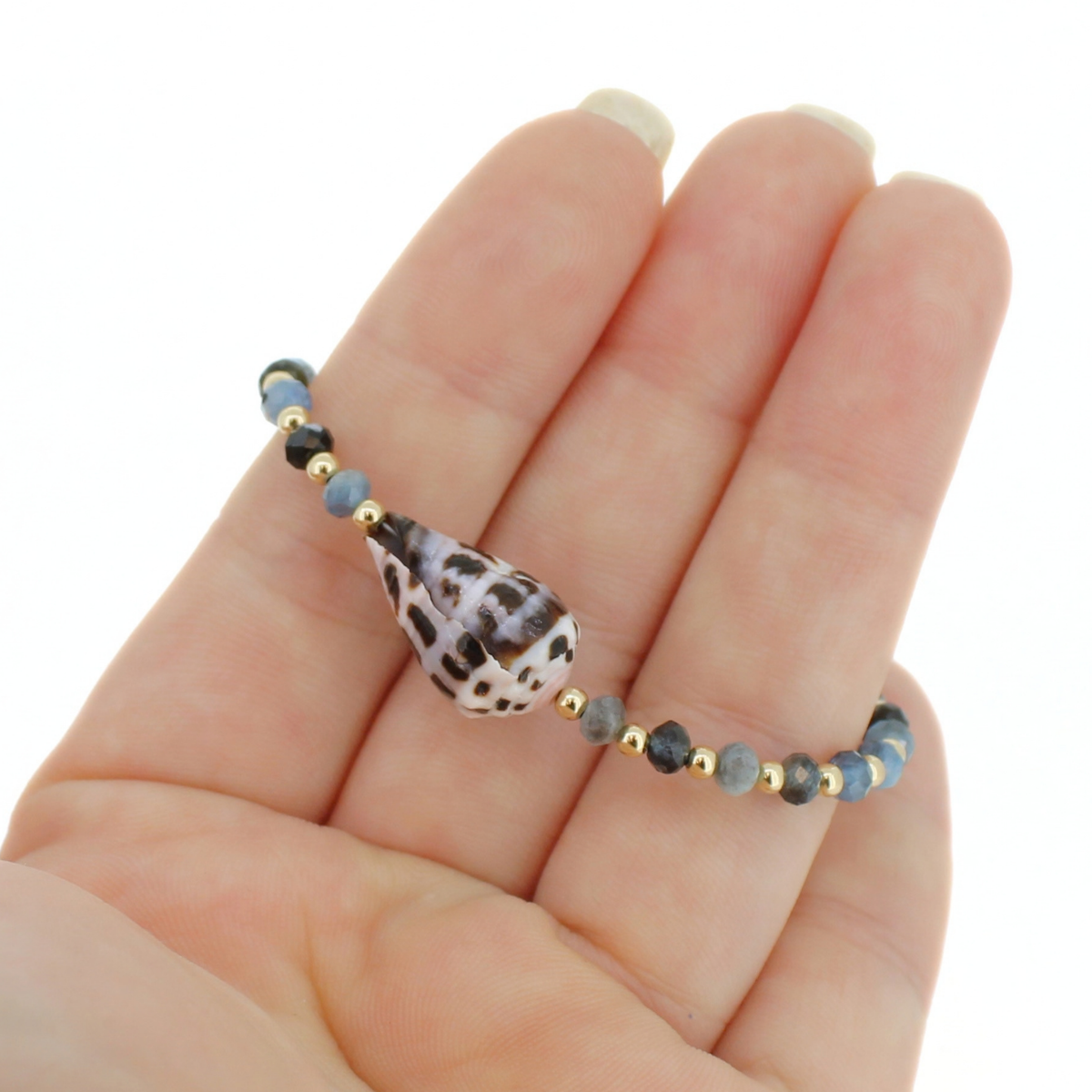 A beaded bracelet with a patterned seashell centerpiece, resting on a person's hand against a white background.