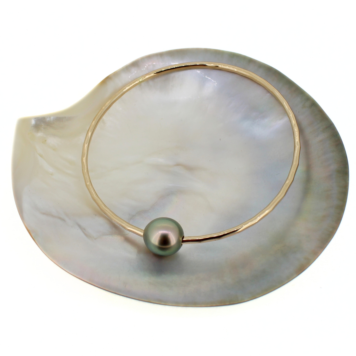 Gold bangle bracelet with a green Tahitian pearl, displayed on a shell against a white background