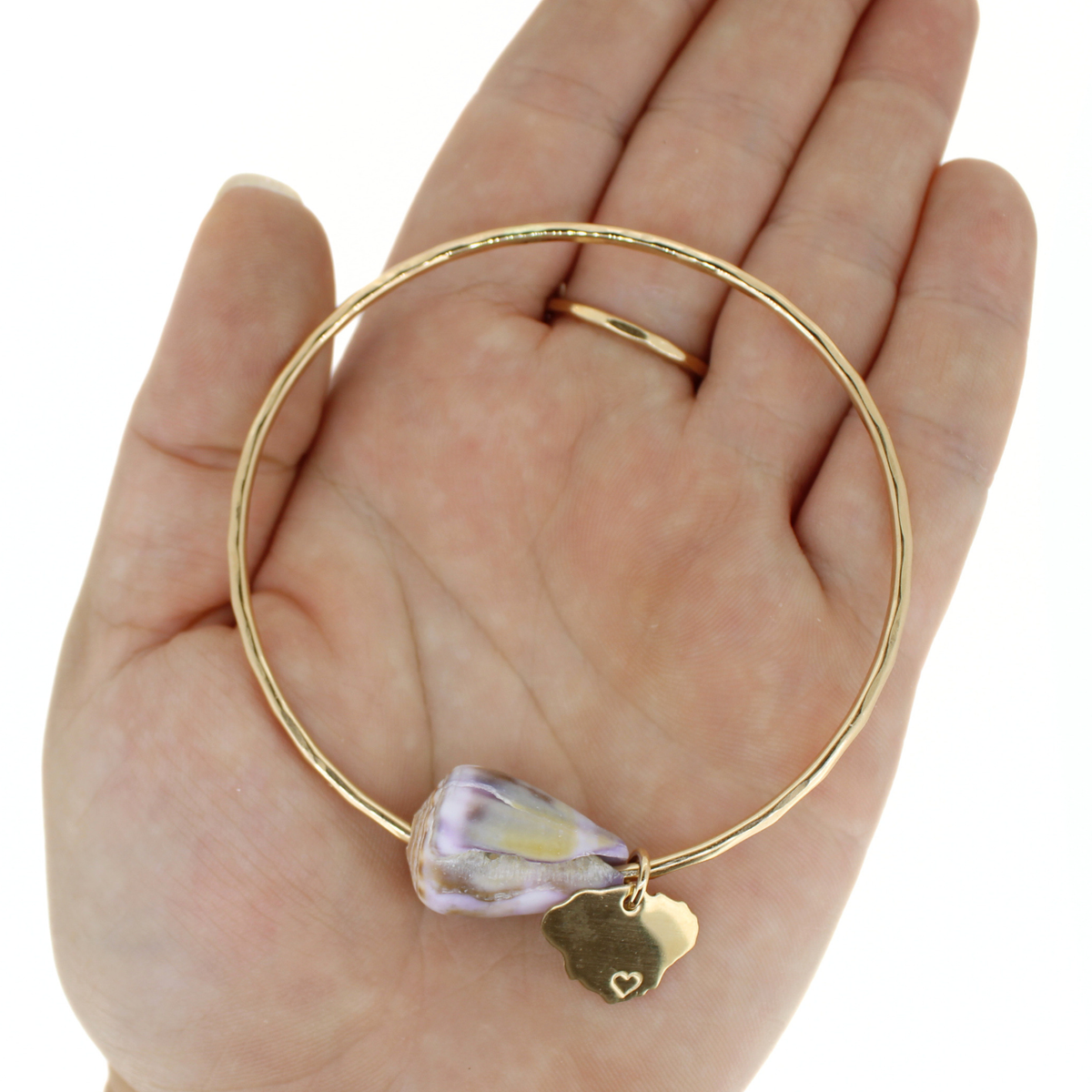 A gold bangle bracelet with a Hawaiian cone shell and a small gold Kauai charm, displayed on a person's hand.