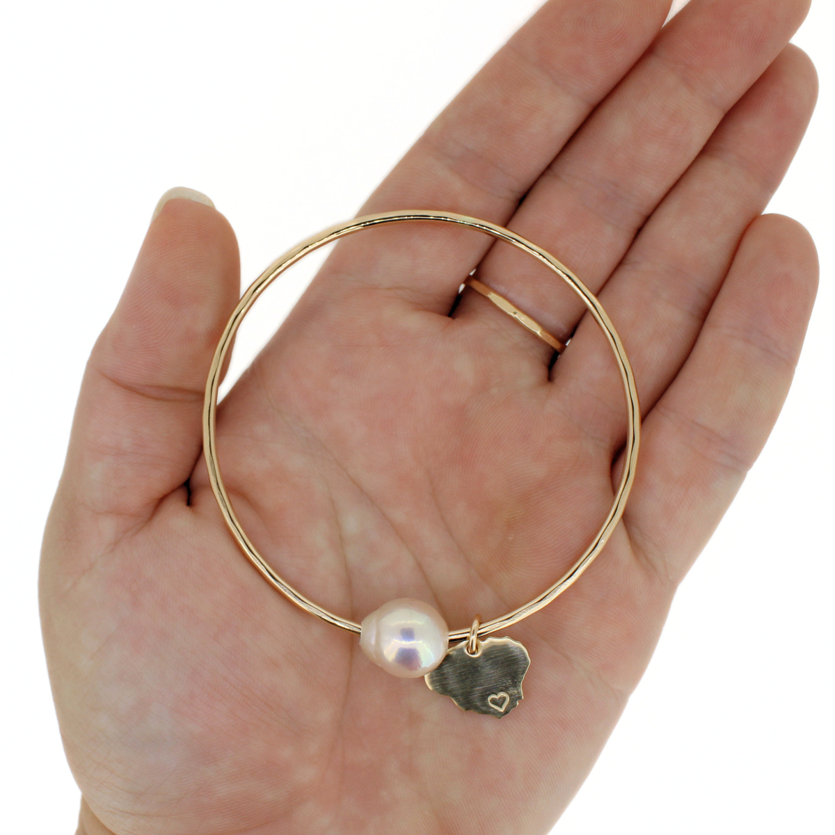 Gold bangle bracelet with white pearl and Kauai island charm displayed on a hand against a white background