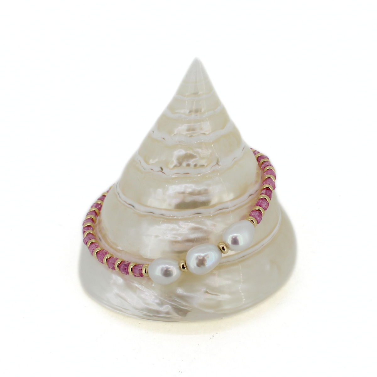 A beaded bracelet with white pearls and pink beads, displayed on a white seashell stand against a white background.