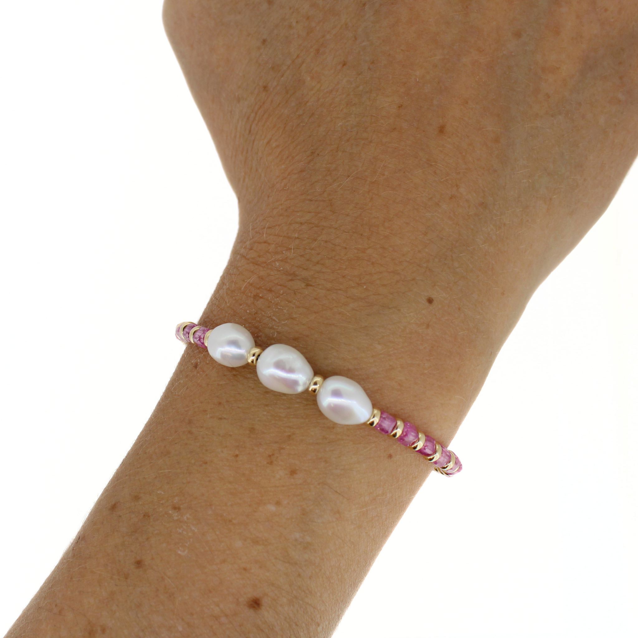 A delicate bracelet worn on a person's wrist, featuring three large white baroque pearls and small pink gemstones set in gold.