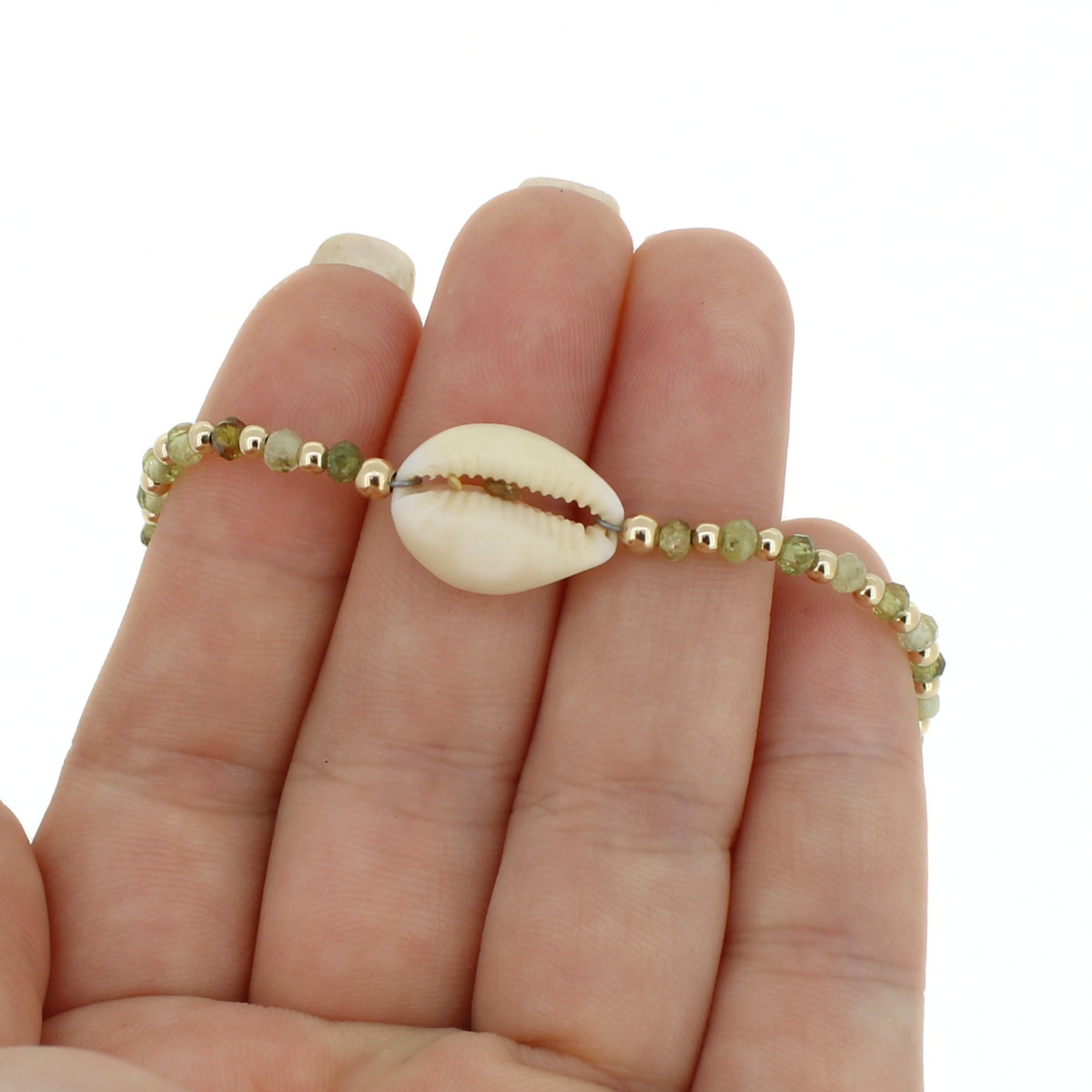 A beaded bracelet with a central cowrie shell, held on a person's fingers against a plain white background.