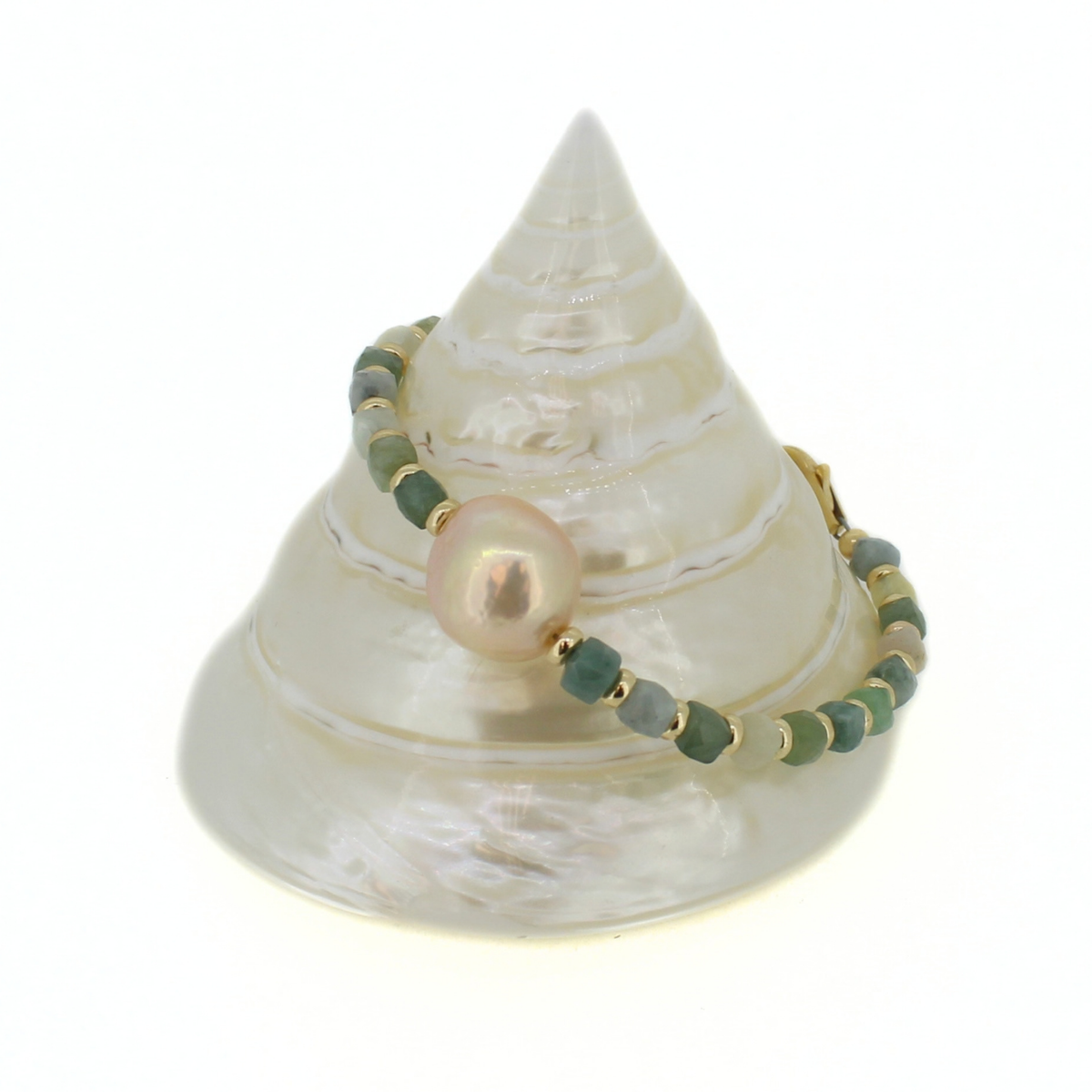A beaded bracelet with green and blue-gray beads, gold spacer rings, and a central iridescent pearl, displayed on a white conical shell stand against a white background.