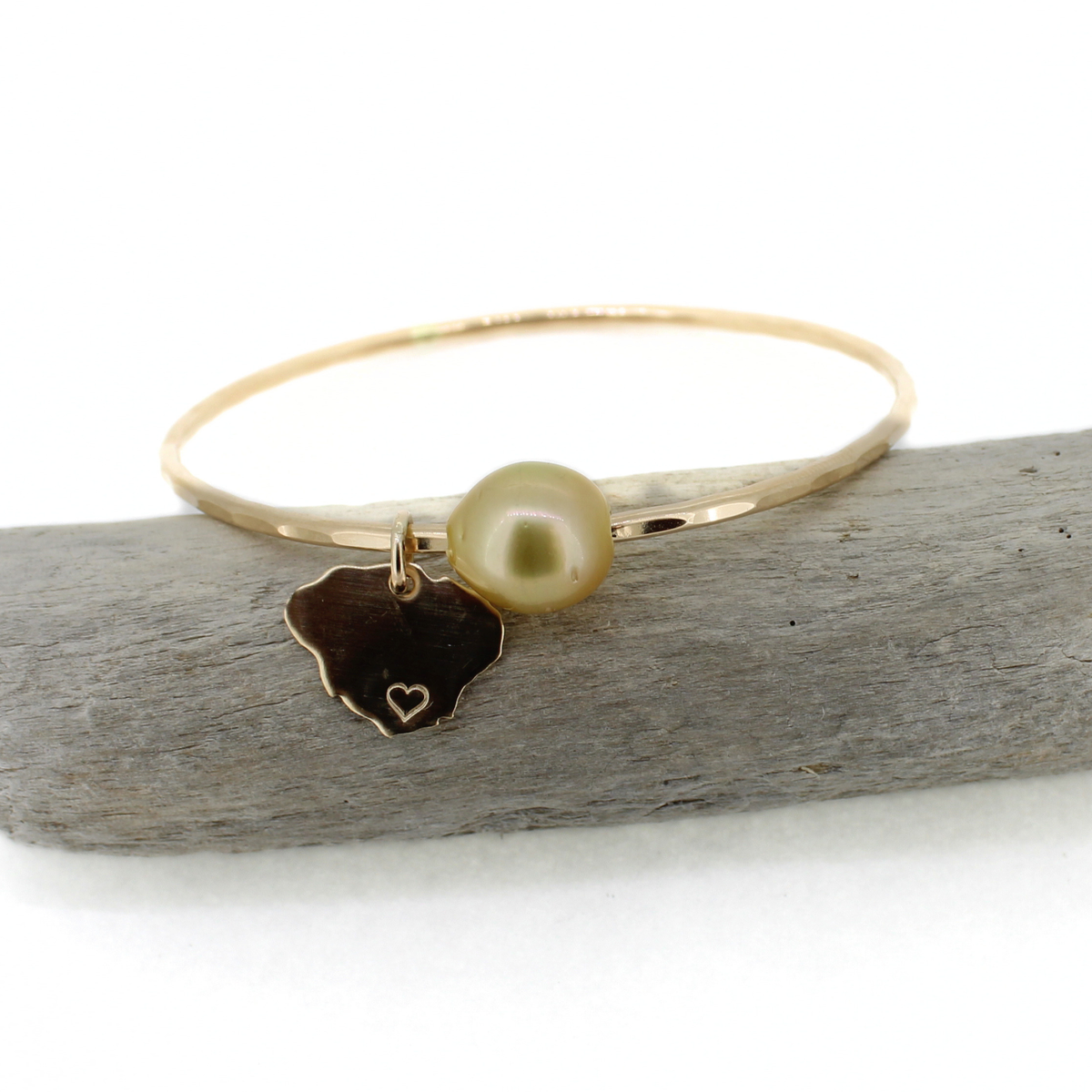 Brianne & Co. gold bangle bracelet with a golden color pearl and Kauai island charm displayed on driftwood