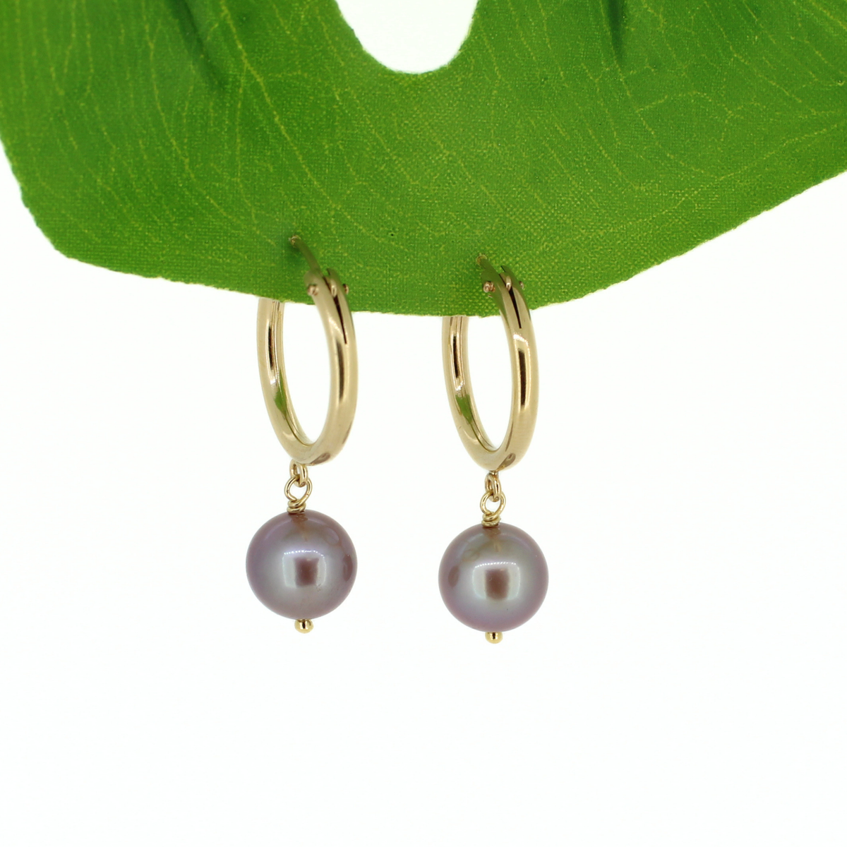 Gold hoop earrings with dangling Edison freshwater pearls, displayed on a green leaf against a white background.