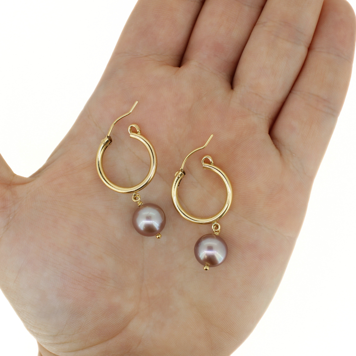 A pair of gold hoop earrings with dangling round pears, displayed on an open hand against a white background.