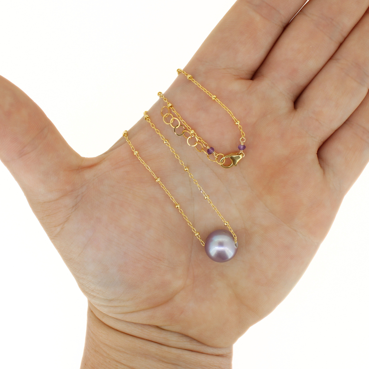 A delicate gold chain necklace with a single lustrous pearl pendant, displayed on an open hand against a plain white background.