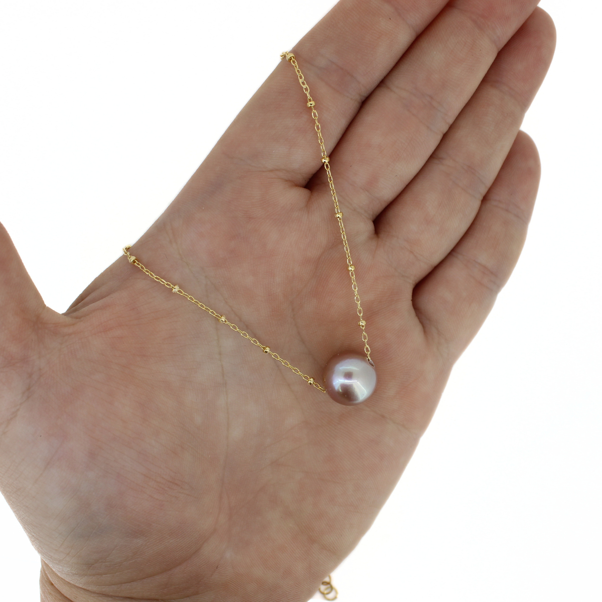 A delicate gold chain necklace with a single round freshwater pearl pendant, displayed on an open hand against a plain white background.
