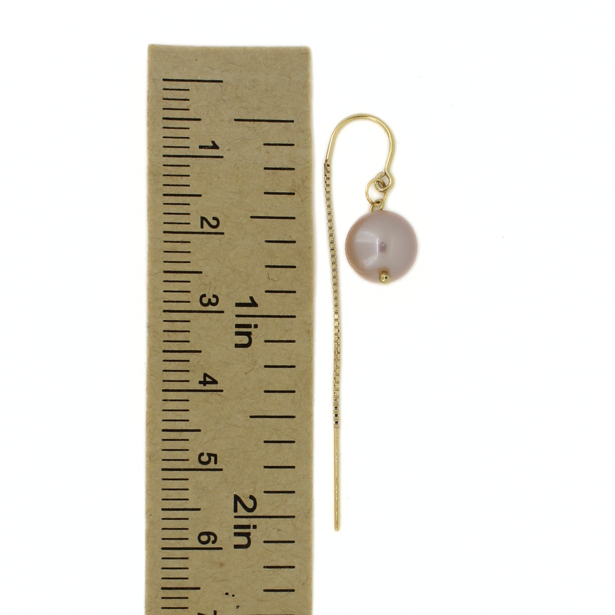 A gold-tone drop earring with a single round pale pink pearl, shown next to a paper ruler for scale on a white background.