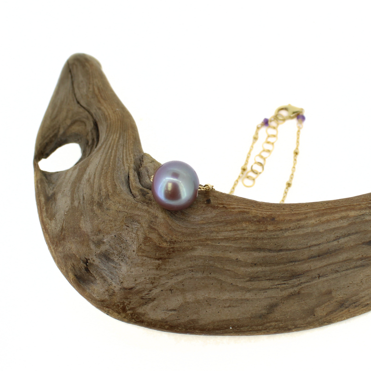 A gold chain necklace with a single iridescent pearl pendant resting on a curved piece of driftwood, photographed against a solid white background.