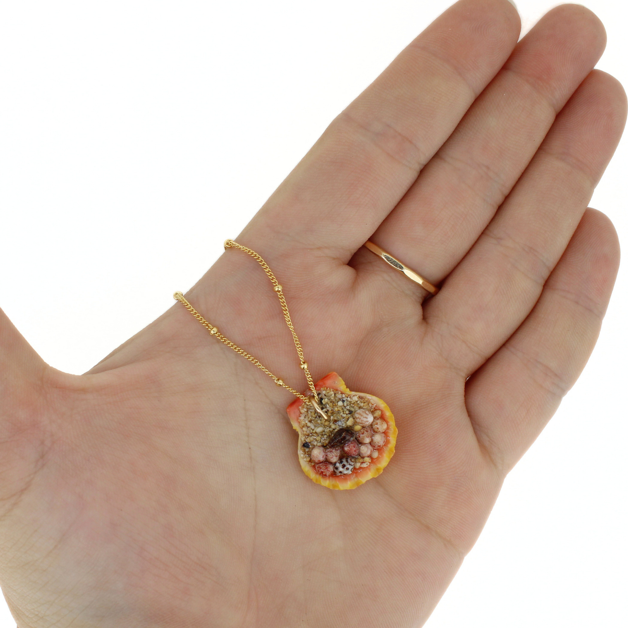 Back side of a sunrise shell pendant showing sand and tiny shells securing the pendant bail
