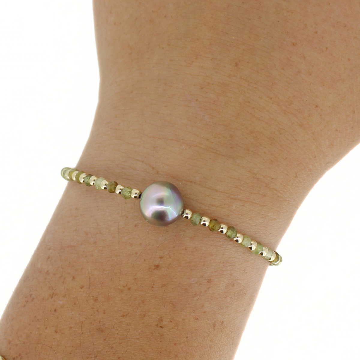 A delicate gold beaded bracelet with a single large, iridescent grey pearl, shown worn on a person's wrist against a white background.