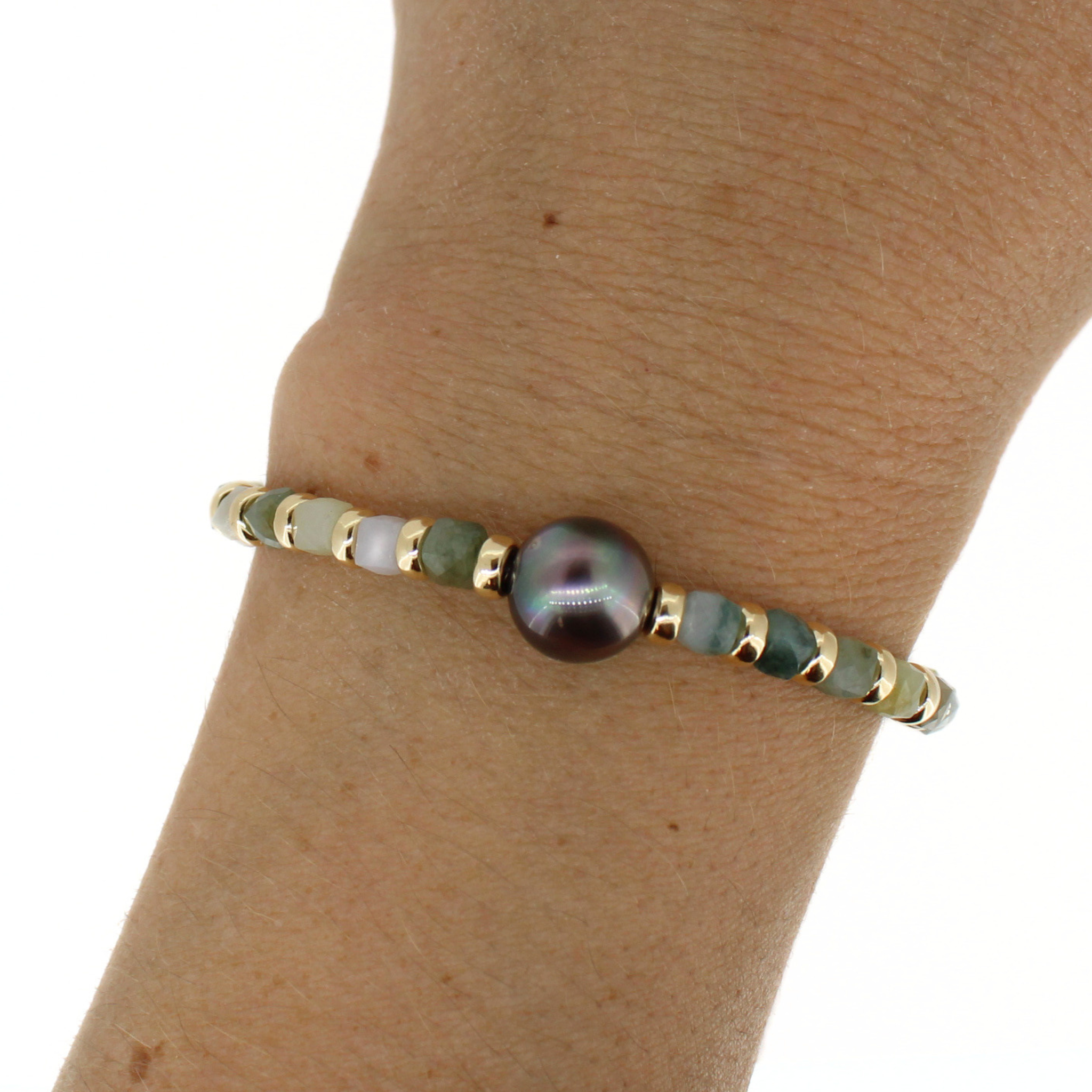 A beaded bracelet with a central iridescent dark pearl, gold spacer beads, and green jade gemstone beads, shown worn on a person's wrist.