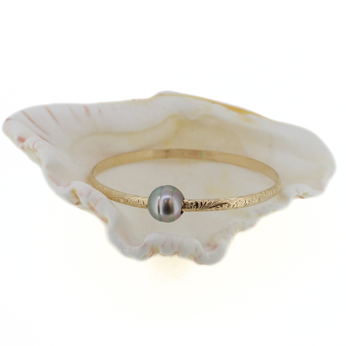 A delicate gold bangle ring featuring a single round, dark gray pearl, displayed on a white clam shell against a white background.
