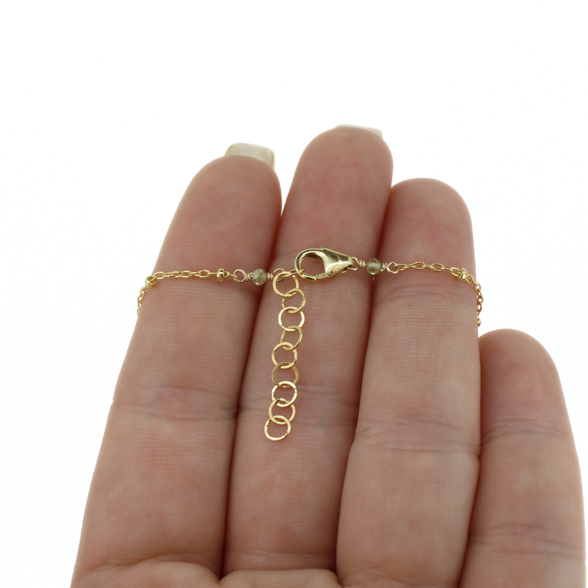 A gold necklace with a lobster clasp, an extender and peridot accent beads.