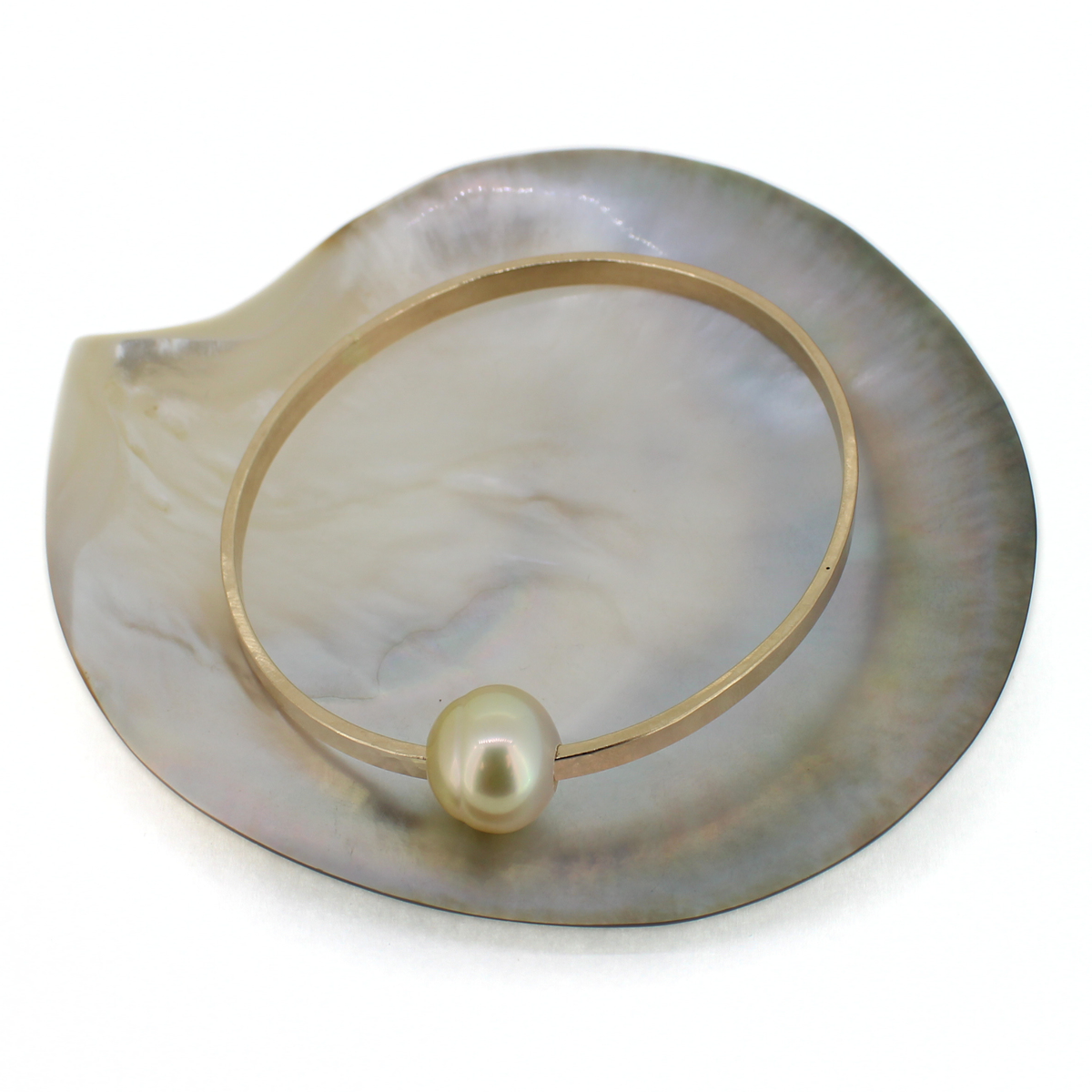 Gold extra thick hammered bangle bracelet with a golden pearl displayed on a shell