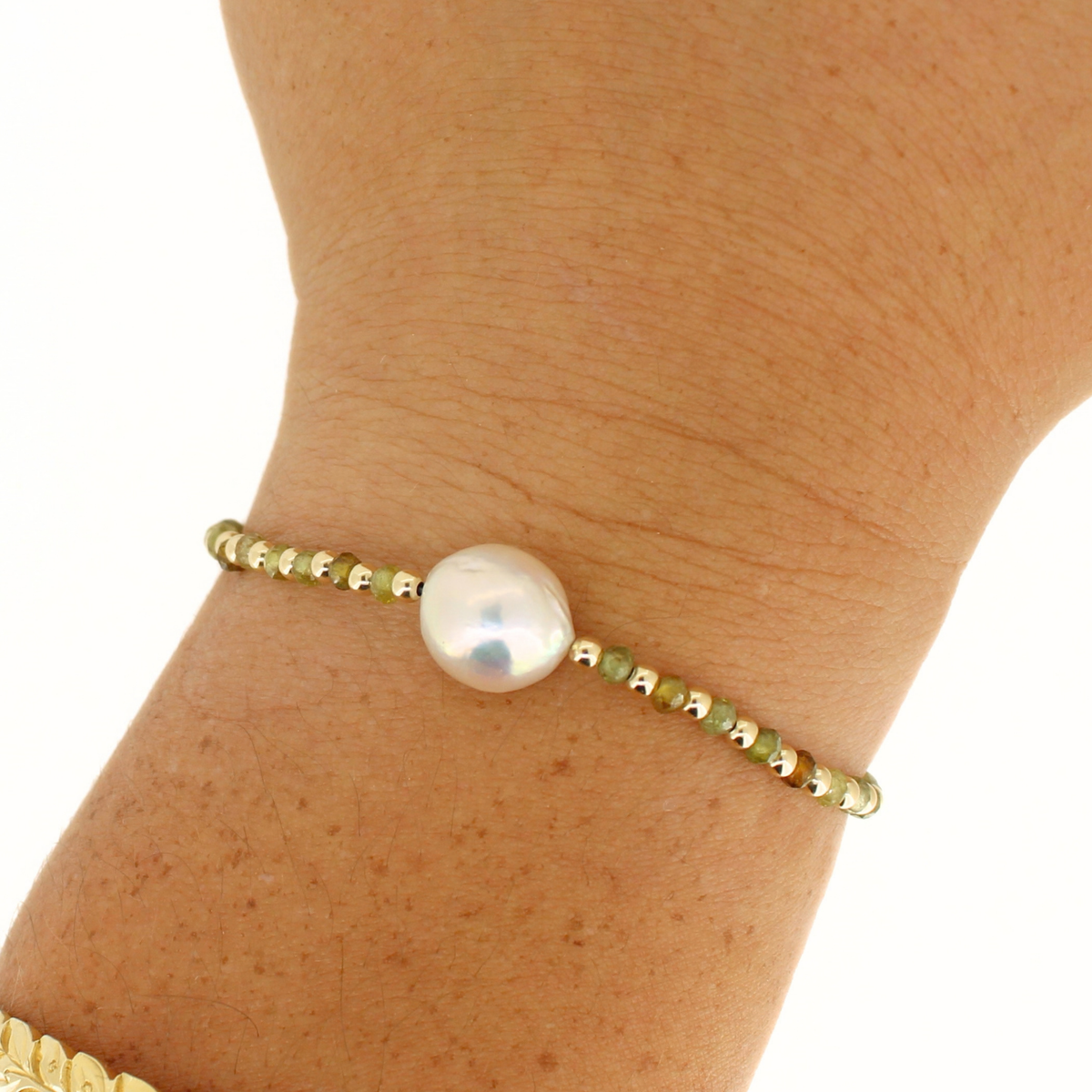 A delicate gold beaded bracelet with a central lustrous white pearl, shown worn on a person's wrist against a plain white background.