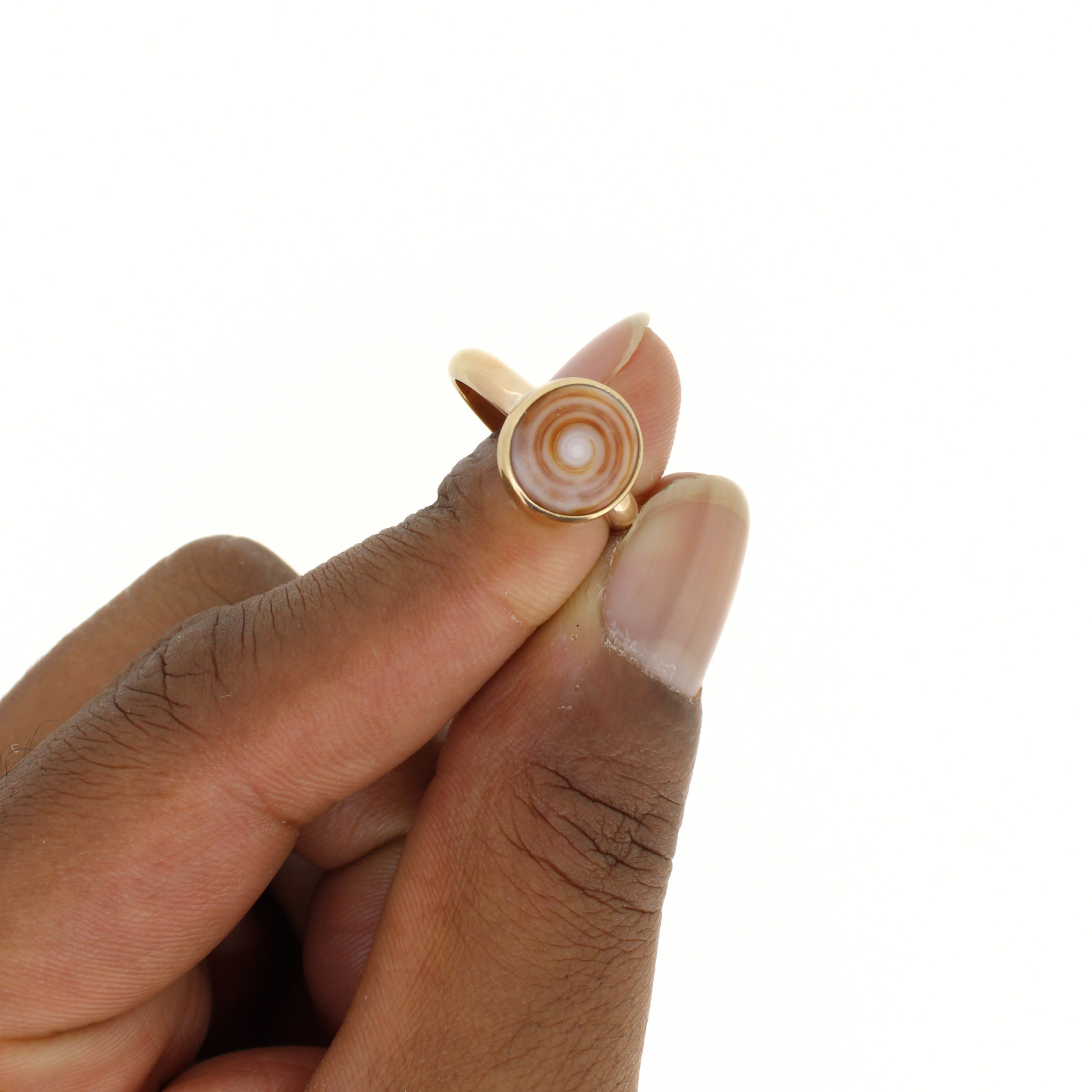 Gold-tone puka shell ring close-up on finger, oval shell with concentric swirls