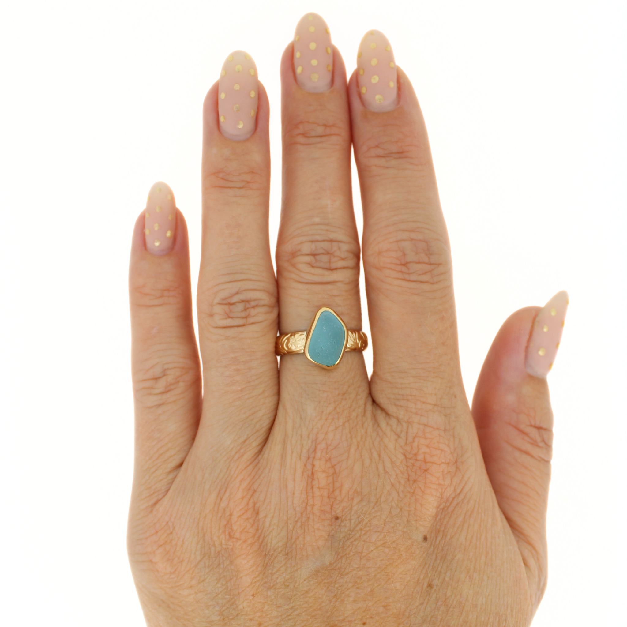 Gold-tone ring with teal sea-glass teardrop bezel worn on finger.