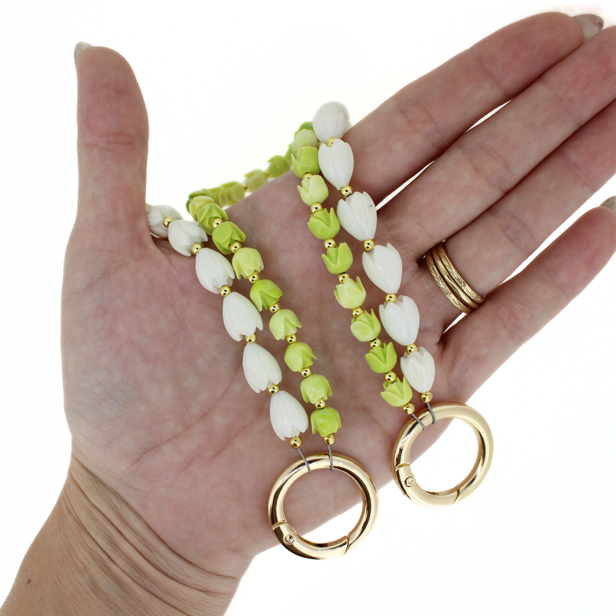 Green and white flower lei keychains with gold rings held in a hand