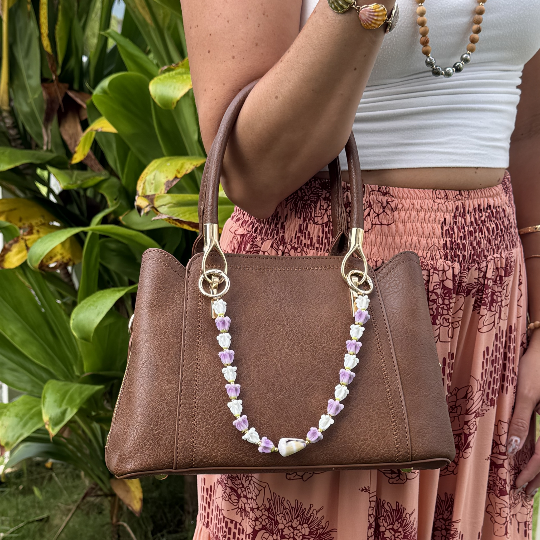 Brown leather tote bag with floral bead shell lei necklace and gold rings